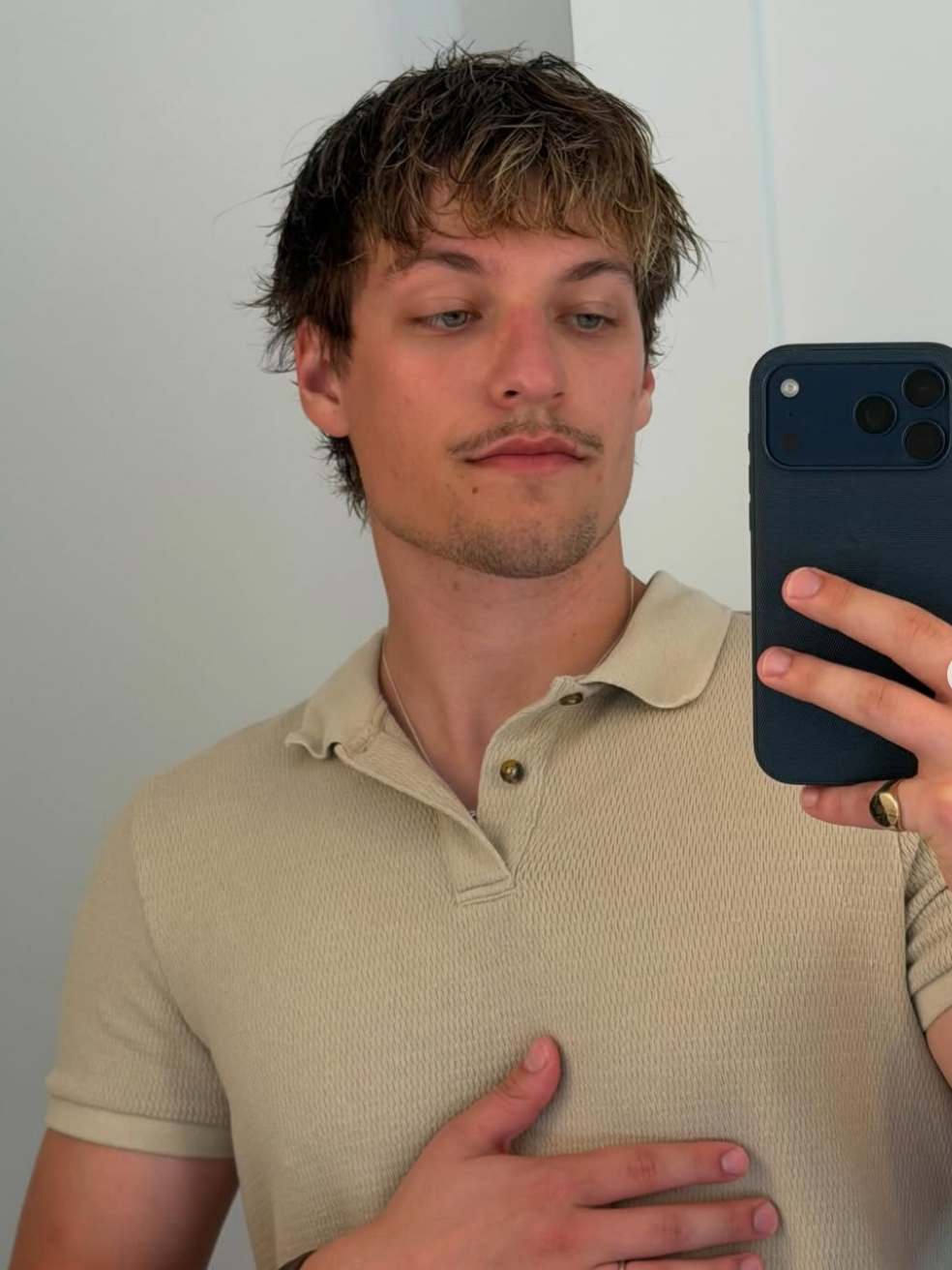 Person taking a reflector selfie, wearing a casual short-sleeve polo shirt, holding a telephone with the different hand