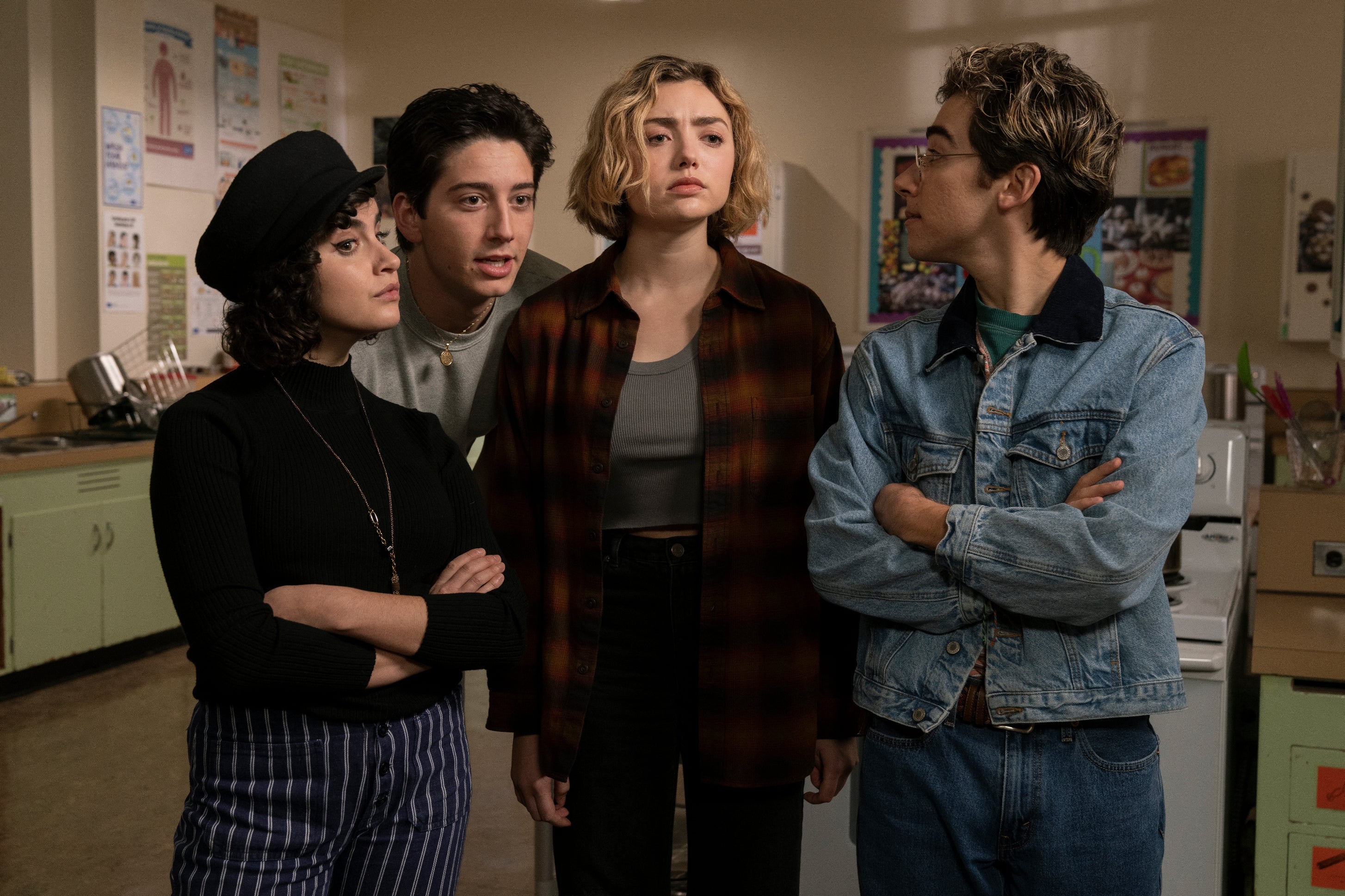 Four young adults stand in a classroom setting, wearing casual attire; one wears a beret, another a plaid jacket, showcasing diverse fashion styles