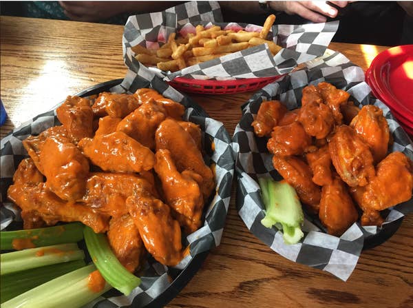 Plates of buffalo wings with celery sticks and a basket of fries on a checkered table