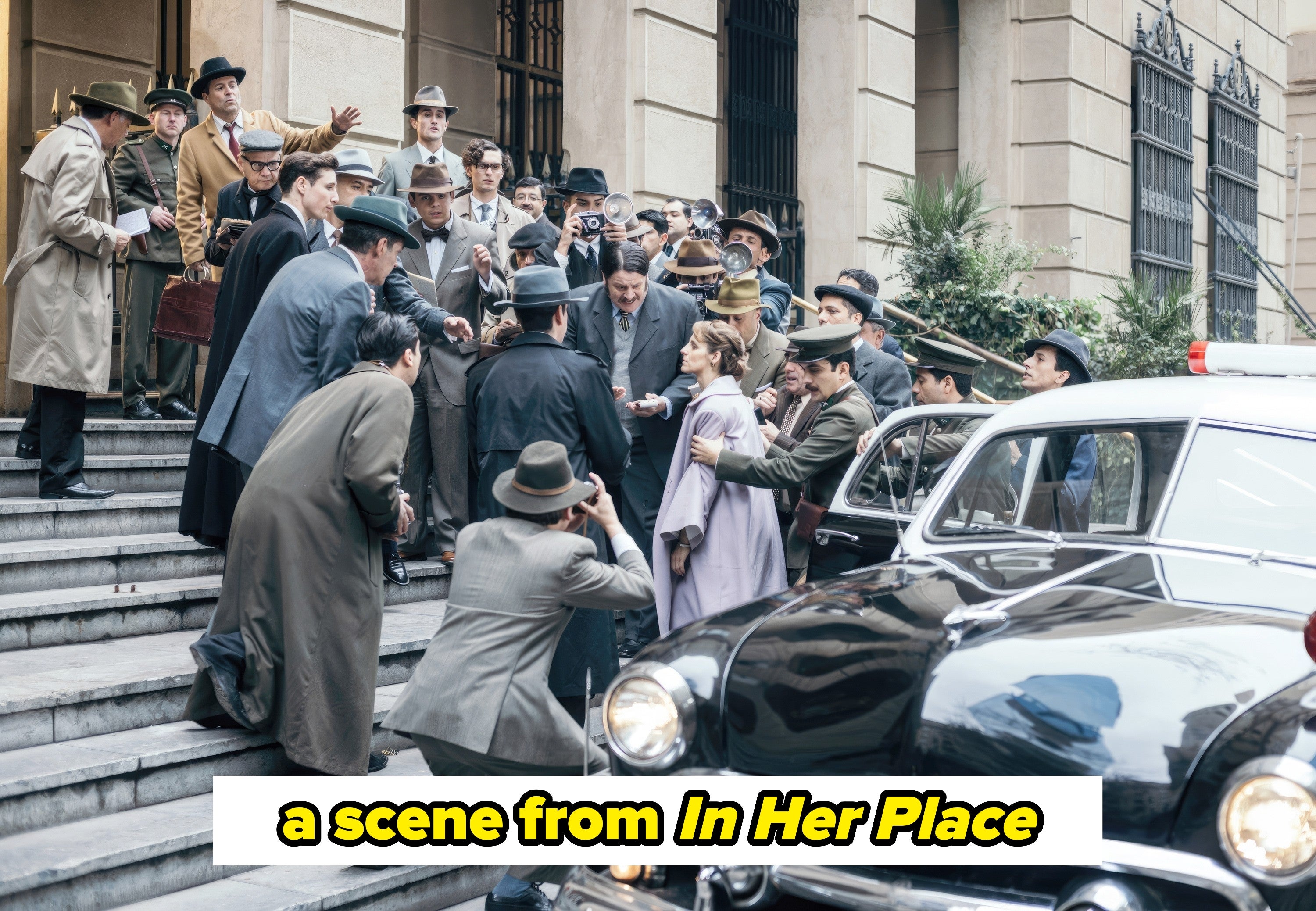 Lewin walking up crowded stairs being hounded by interviewers in a scene from "In Her Place"