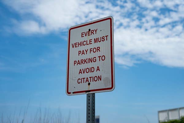 Sign with the text: "Every vehicle must pay for parking to avoid a citation," against a sky backdrop