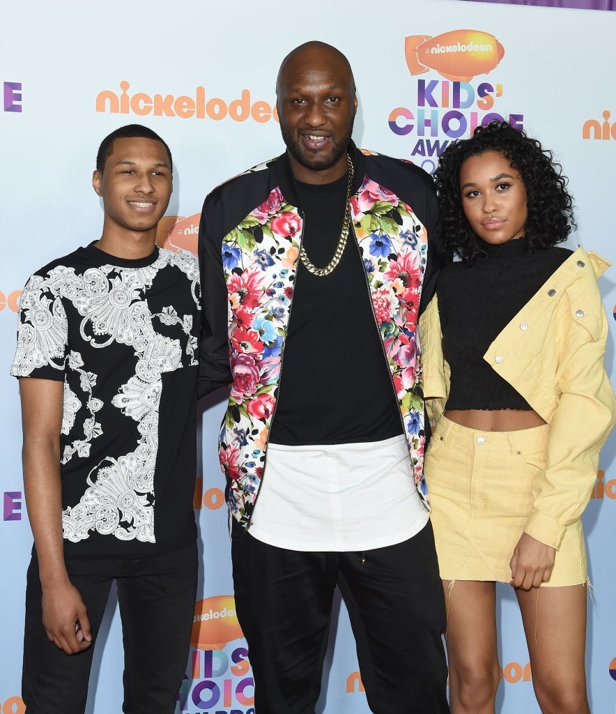 Three individuals airs astatine an event; the halfway idiosyncratic wears a floral jacket, portion the others athletics casual black-and-white and light-colored outfits