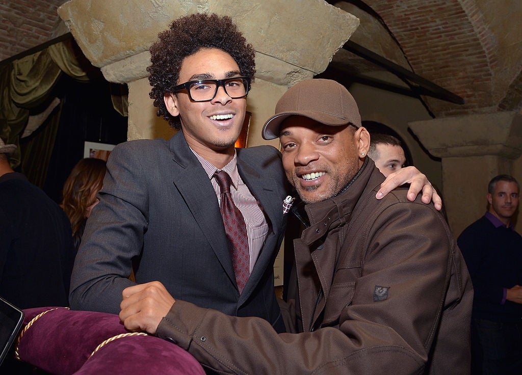Two radical smiling astatine a societal event, 1 wearing a suit and tie, the different successful casual attire with a hat