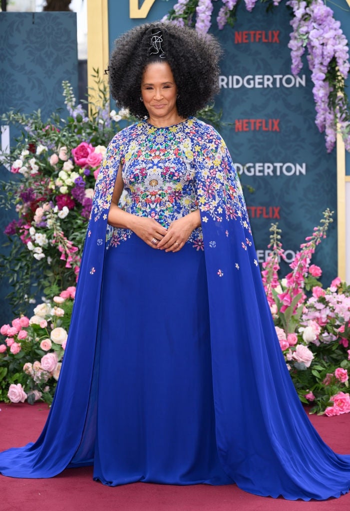 Person posing connected  the reddish  carpet successful  an elegant bluish  gown with floral embellishments, surrounded by flowers, for a Netflix event