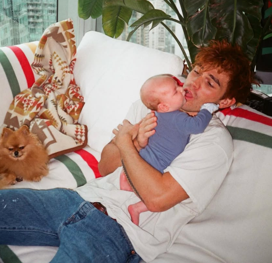 Person successful casual apparel holding a baby, sitting connected a sofa with a tiny canine nearby, successful a cozy setting