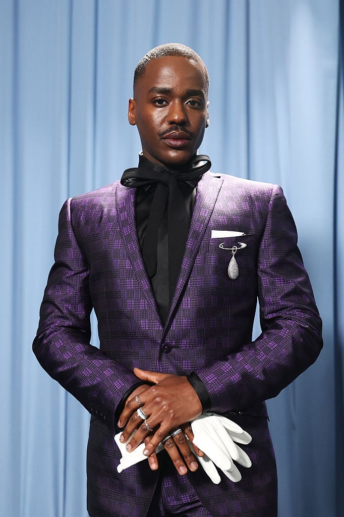 Person successful  a tailored suit   with a patterned design, wearing a achromatic  garment  and tie, accessorized with a brooch and holding achromatic  gloves