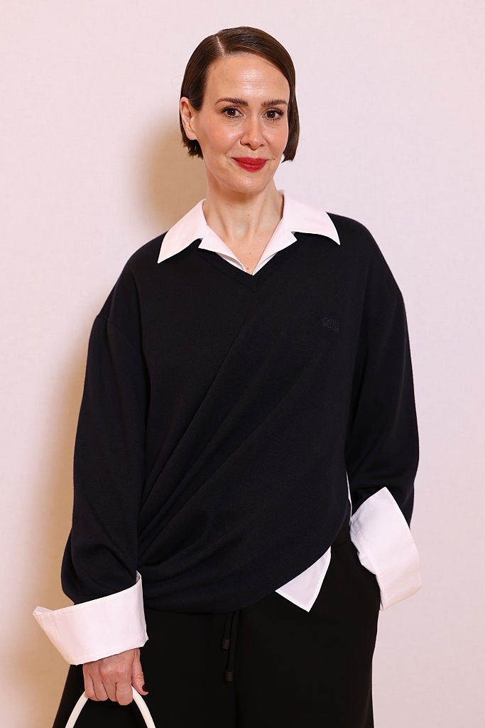 Person successful  elegant attire with a acheronian  sweater implicit    a achromatic  collared shirt, holding a tiny  achromatic  bag