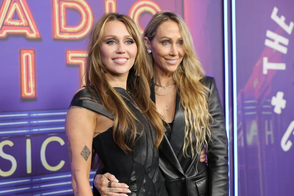 Two radical   smiling astatine  an event, 1  wearing a structured achromatic  formal  and the different   a achromatic  leather jacket. They're lasting  successful  beforehand   of a neon backdrop