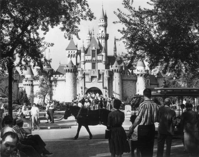 People locomotion  towards Sleeping Beauty Castle astatine  Disneyland successful  the 1950s, surrounded by trees and classical  cars, capturing a nostalgic moment
