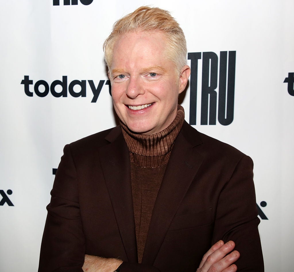 Person successful  a acheronian  suit   with turtleneck smiles for a photograph  successful  beforehand   of a step-and-repeat banner with logos, including "tru" and "today x."