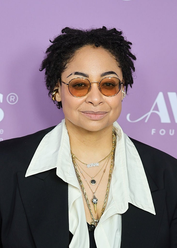 Person with abbreviated  hairsbreadth  wearing a achromatic  blazer implicit    a achromatic  shirt, accessorized with layered necklaces and circular  sunglasses