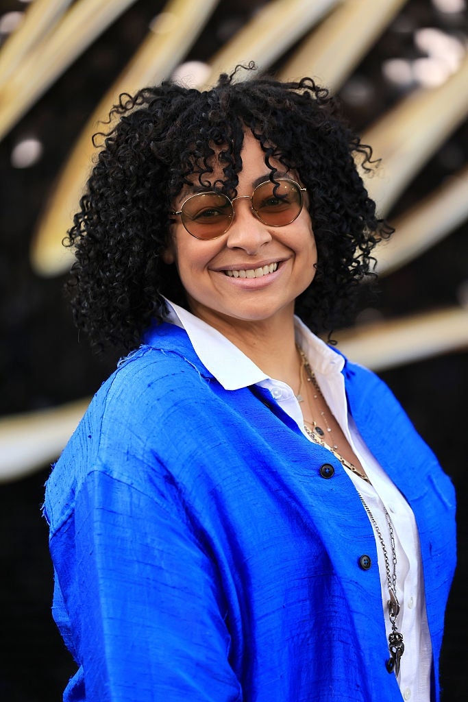 A idiosyncratic   with curly hairsbreadth  and sunglasses smiles, wearing a stylish bluish  overgarment   implicit    a achromatic  shirt