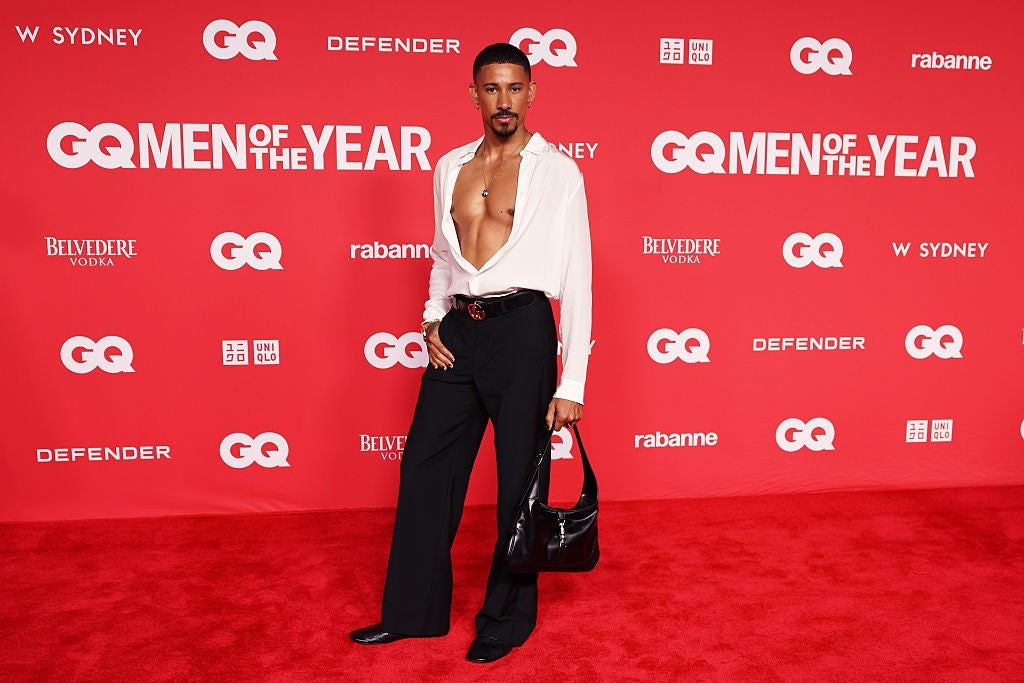 Person connected  reddish  carpet successful  a bold outfit with a heavy  V-neck shirt, wide-leg pants, and holding a handbag, posing confidently for the camera
