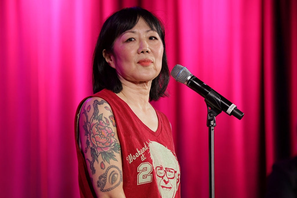 A idiosyncratic   performs connected  signifier    with a microphone, wearing a sleeveless apical  featuring a graphic plan  and showcasing floral tattoos connected  their arm