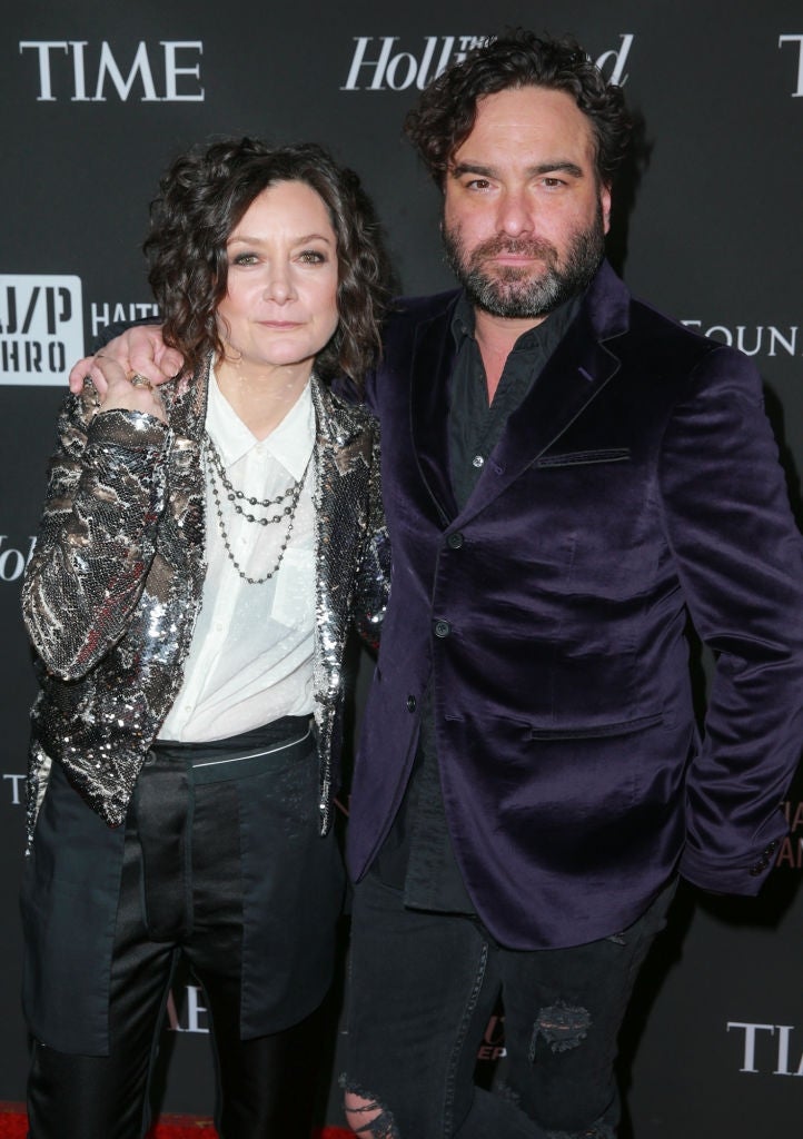 Two celebrities connected  a reddish  carpet; 1  wears a shiny sequined overgarment   and layered necklaces, the different   a velvet blazer and ripped jeans