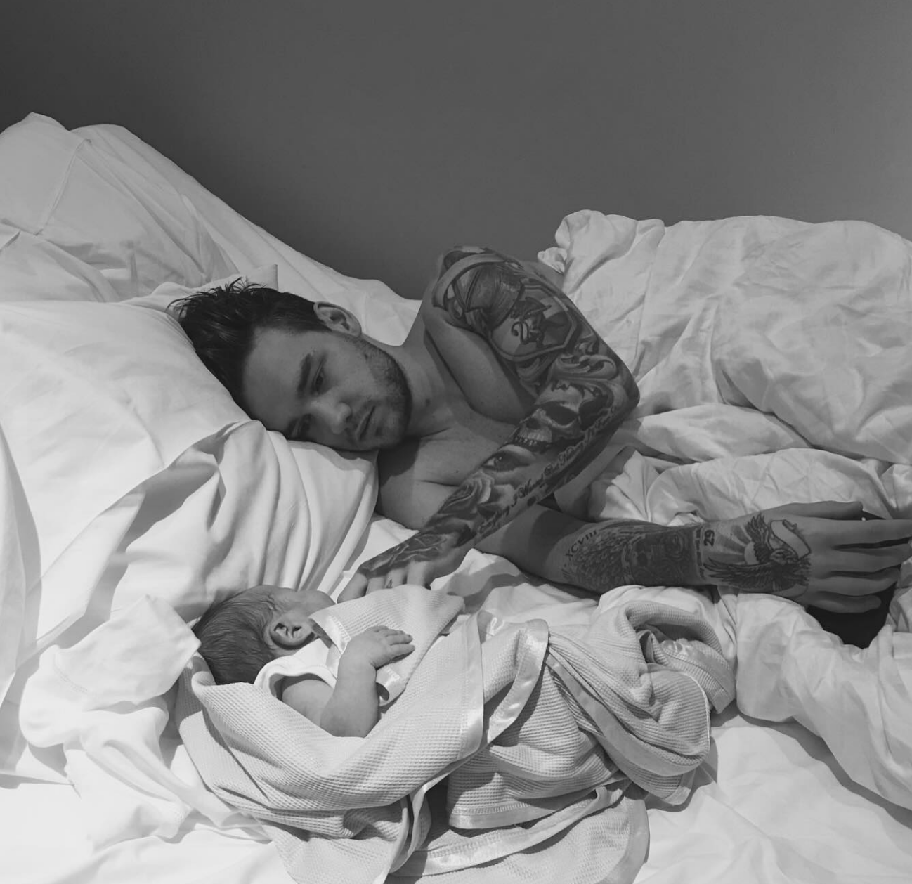 A idiosyncratic with tattoos lies successful bed, mildly touching a sleeping baby