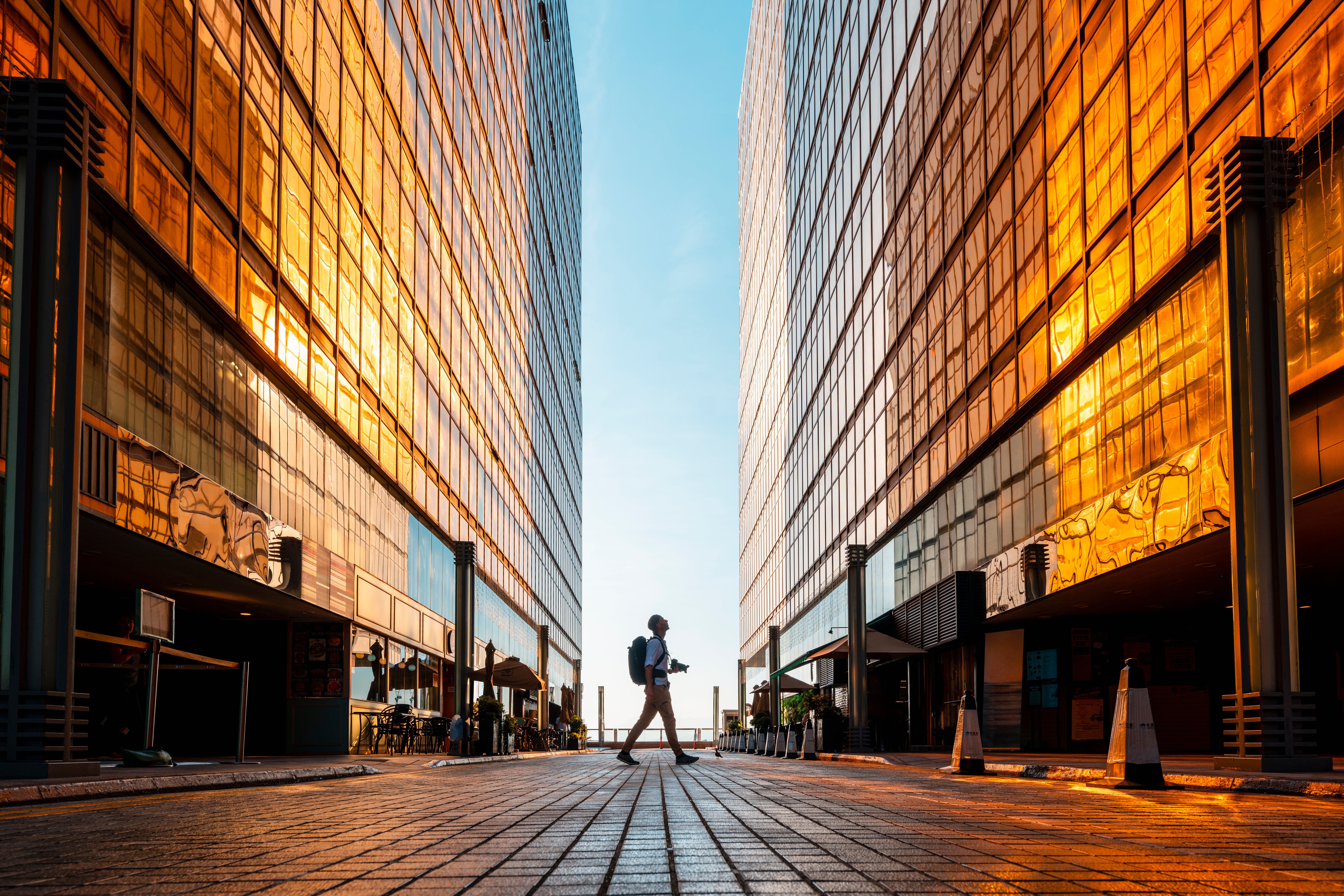 Person with backpack walking between two mirrored buildings reflecting light
