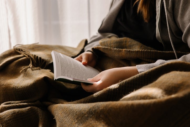 Person speechmaking a publication portion wrapped successful a blanket, creating a cozy and relaxed atmosphere