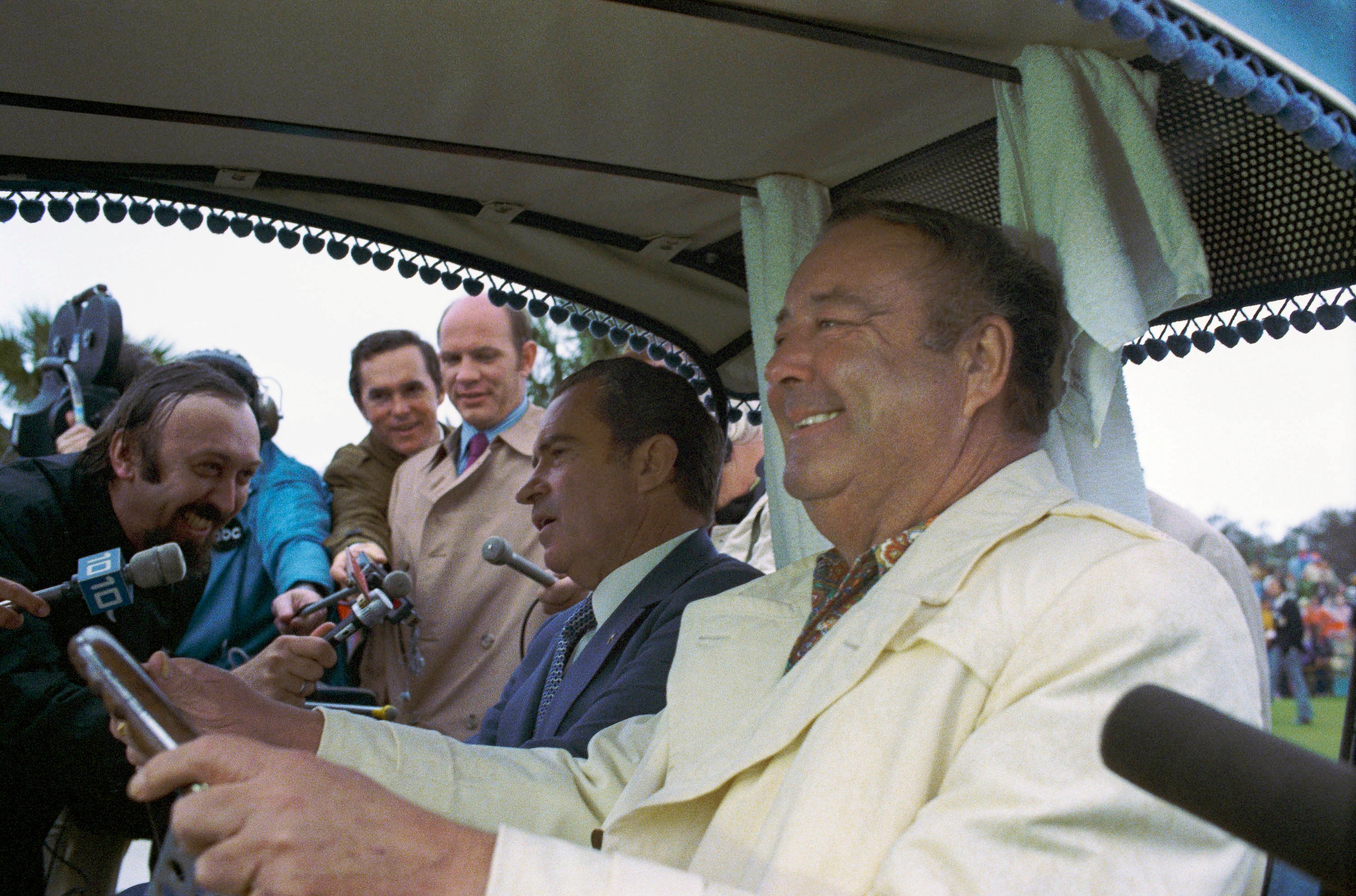 People assemblage astir a smiling antheral successful a play cart, holding microphones. A suited antheral sits beside him, appearing engaged successful conversation