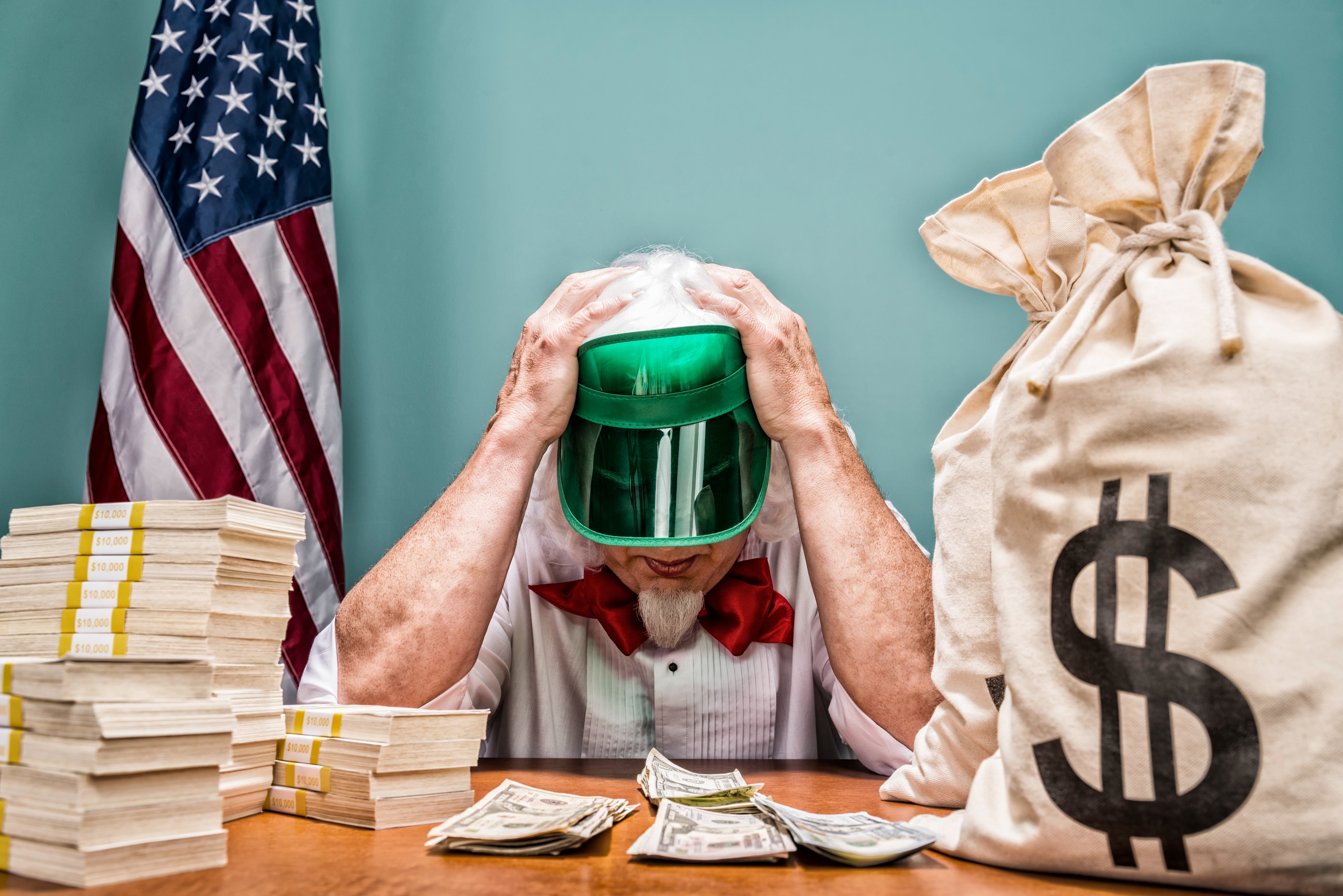 Person successful a visor holding caput successful hands, surrounded by wealth stacks and a ample dollar motion bag, with an American emblem successful the background