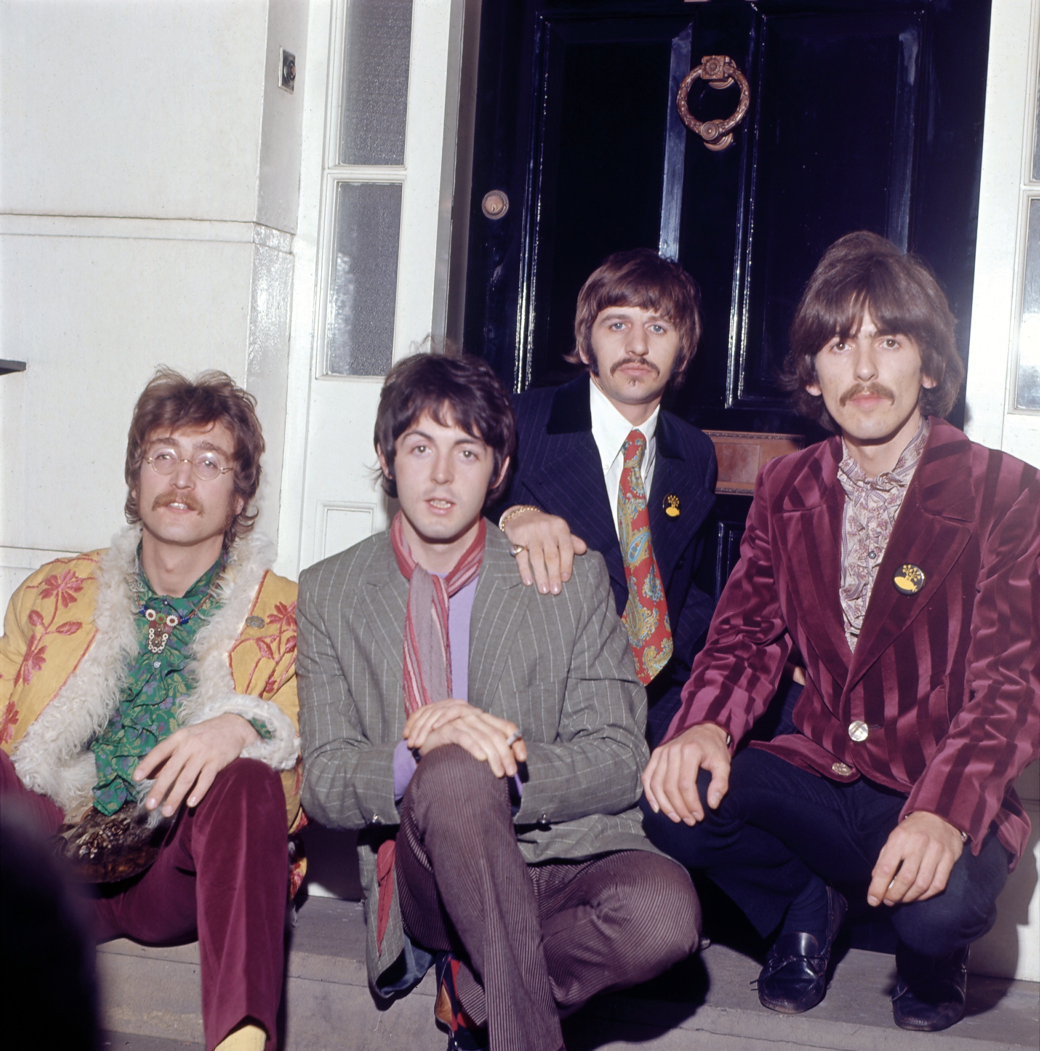 Four men successful 1960s manner with colorful suits and scarves seated connected steps successful beforehand of a door