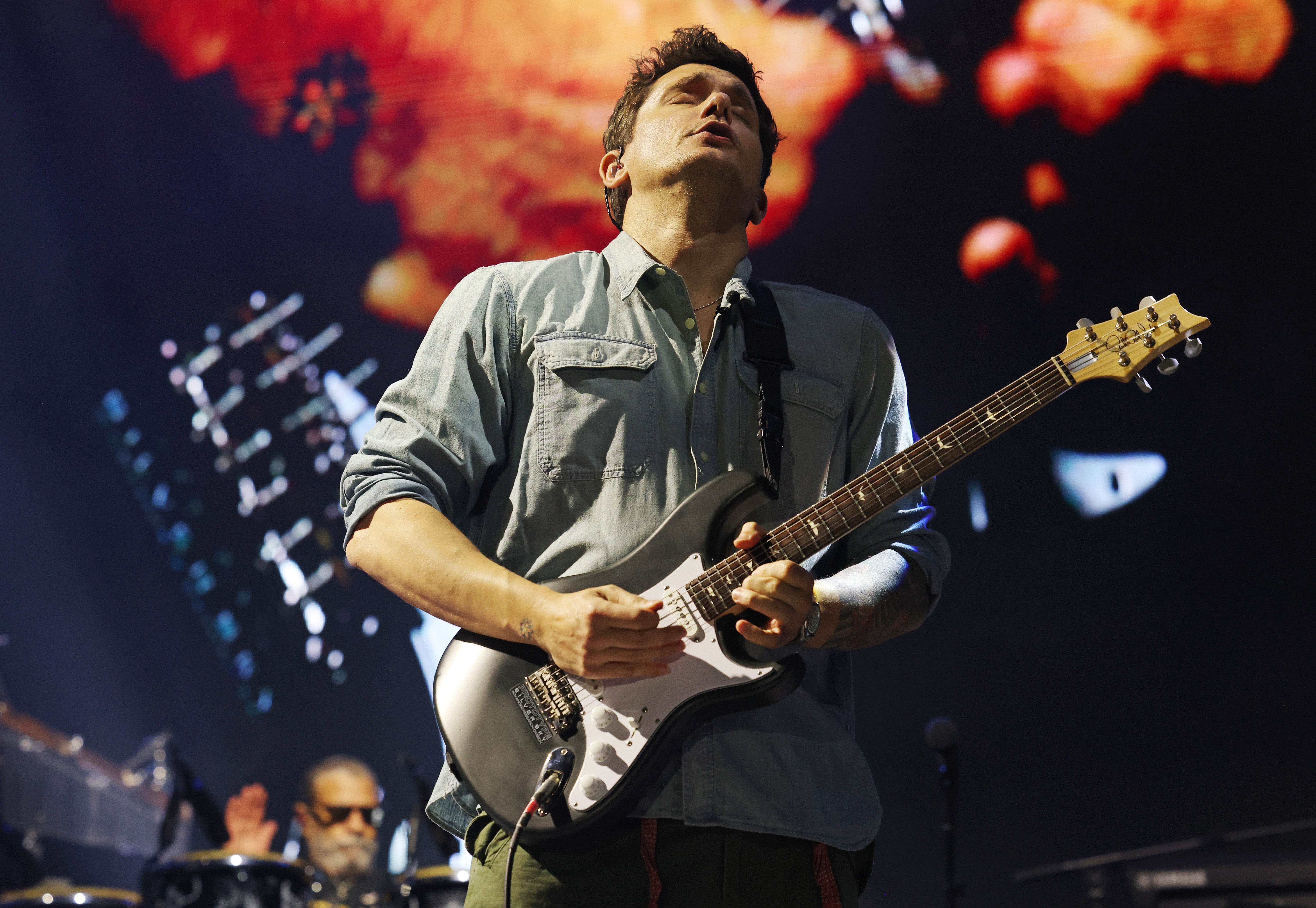 Musician passionately playing electric guitar on stage during a live performance, wearing a casual shirt