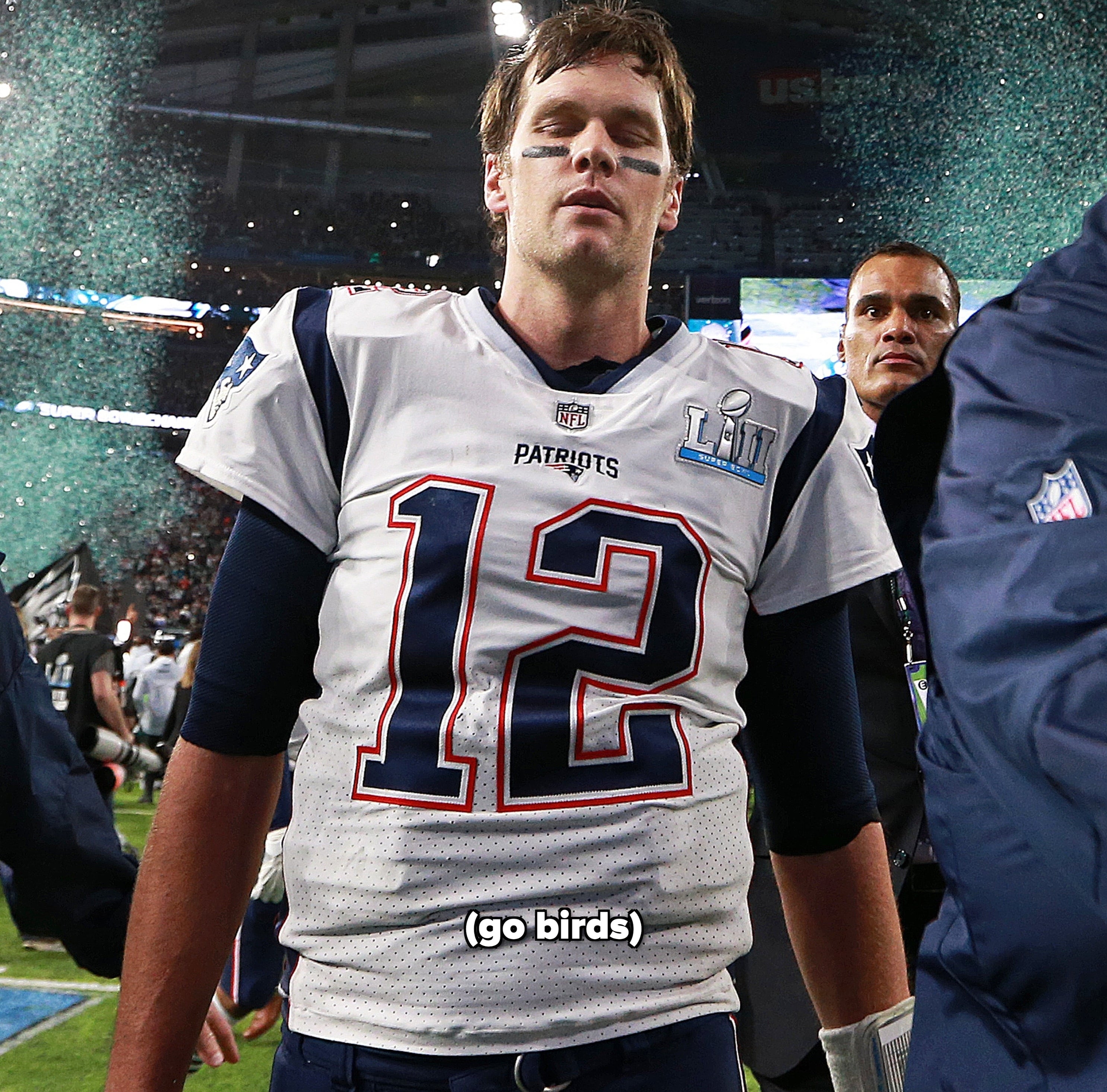 Tom Brady closing his eyes in disappointment while walking off the field after Super Bowl 52 with green confetti in the background for the Eagles victory
