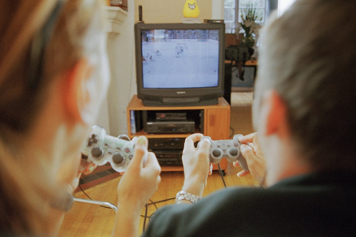 Two people playing a hockey video game on a TV, holding game controllers, focused on the screen