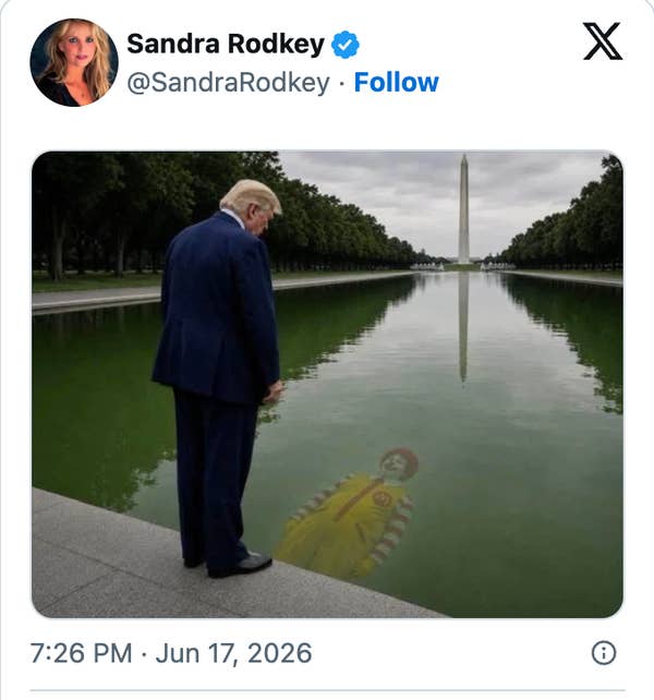 A man in a suit stands by a reflecting pool, seeing an image of a clown in the water. Washington Monument is visible in the background