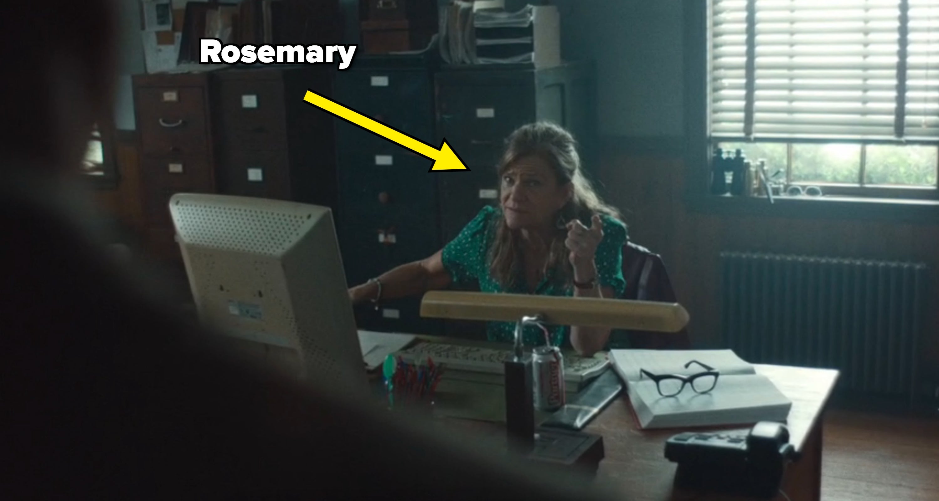 Woman sitting astatine  a table  with machine  and paperwork, looking attentive. Office mounting  with filing cabinets and model   blinds successful  the background