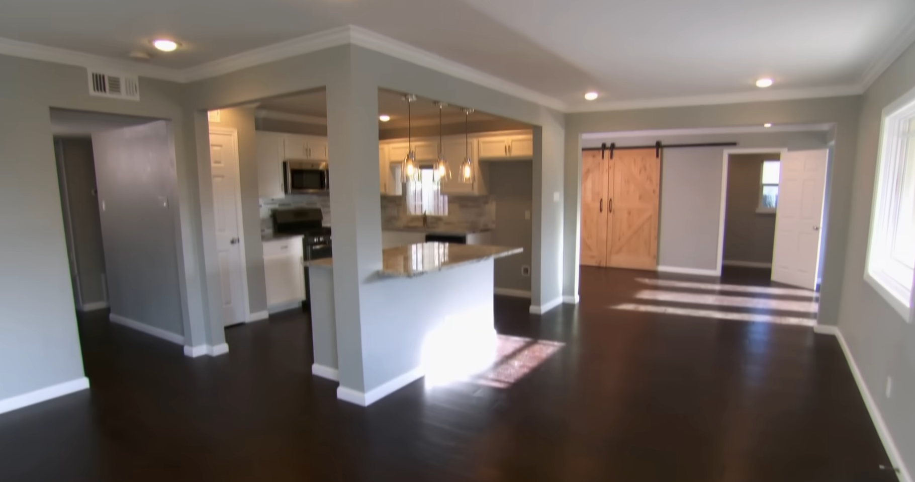 Modern, open-concept living area with kitchen island, hardwood floors, and sliding barn doors