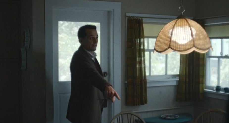 A idiosyncratic   successful  a suit   stands successful  a vintage-style country   with a wicker lampshade, pointing towards thing  off-camera