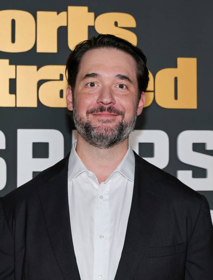 Alexis Ohanian with short hair and a beard wears a suit, posing in front of a "Sports Illustrated" backdrop