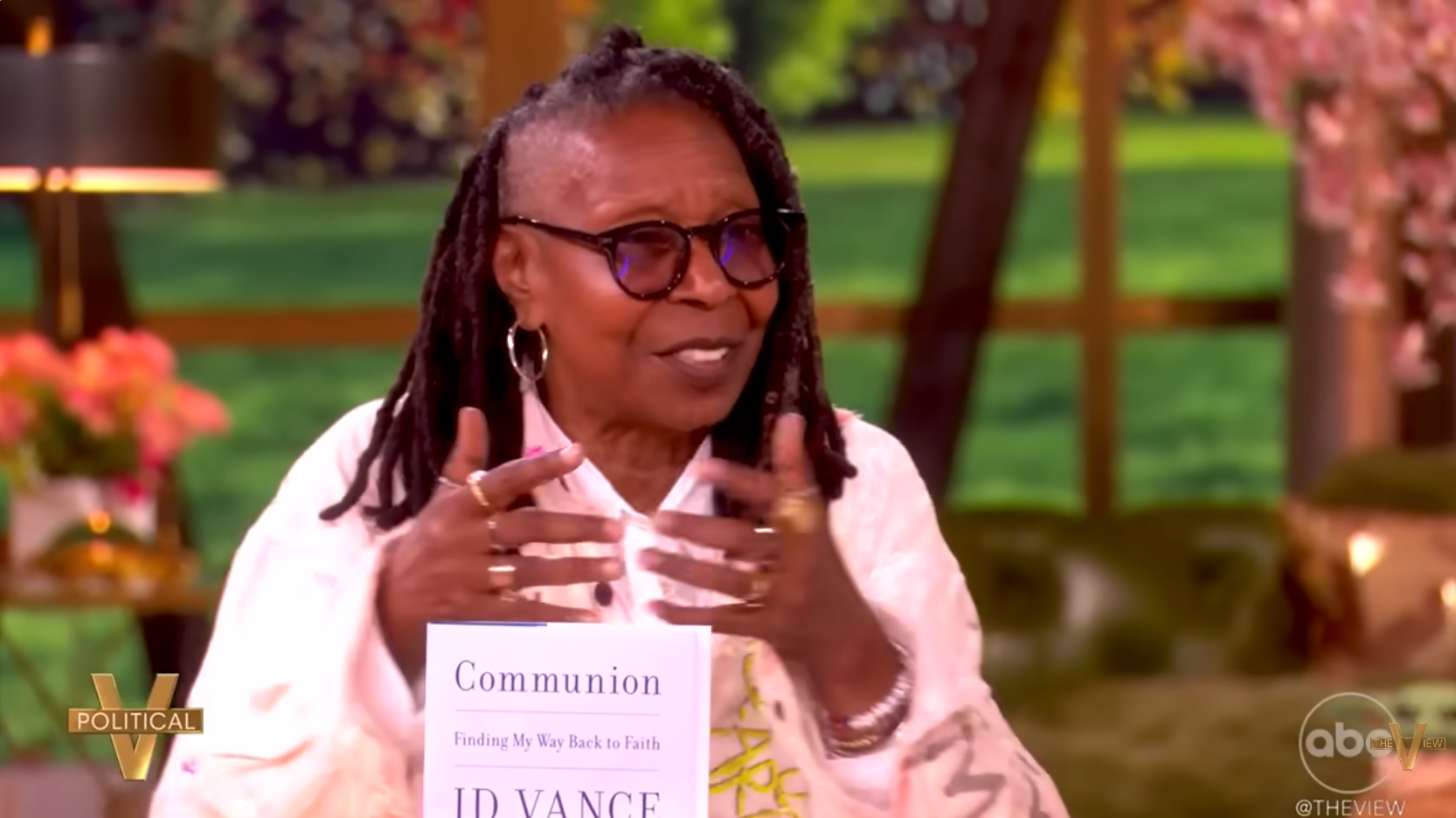Person speaking on a talk show, wearing glasses and a light jacket. They're discussing the book "Communion: Finding My Way Back to Faith" by JD Vance