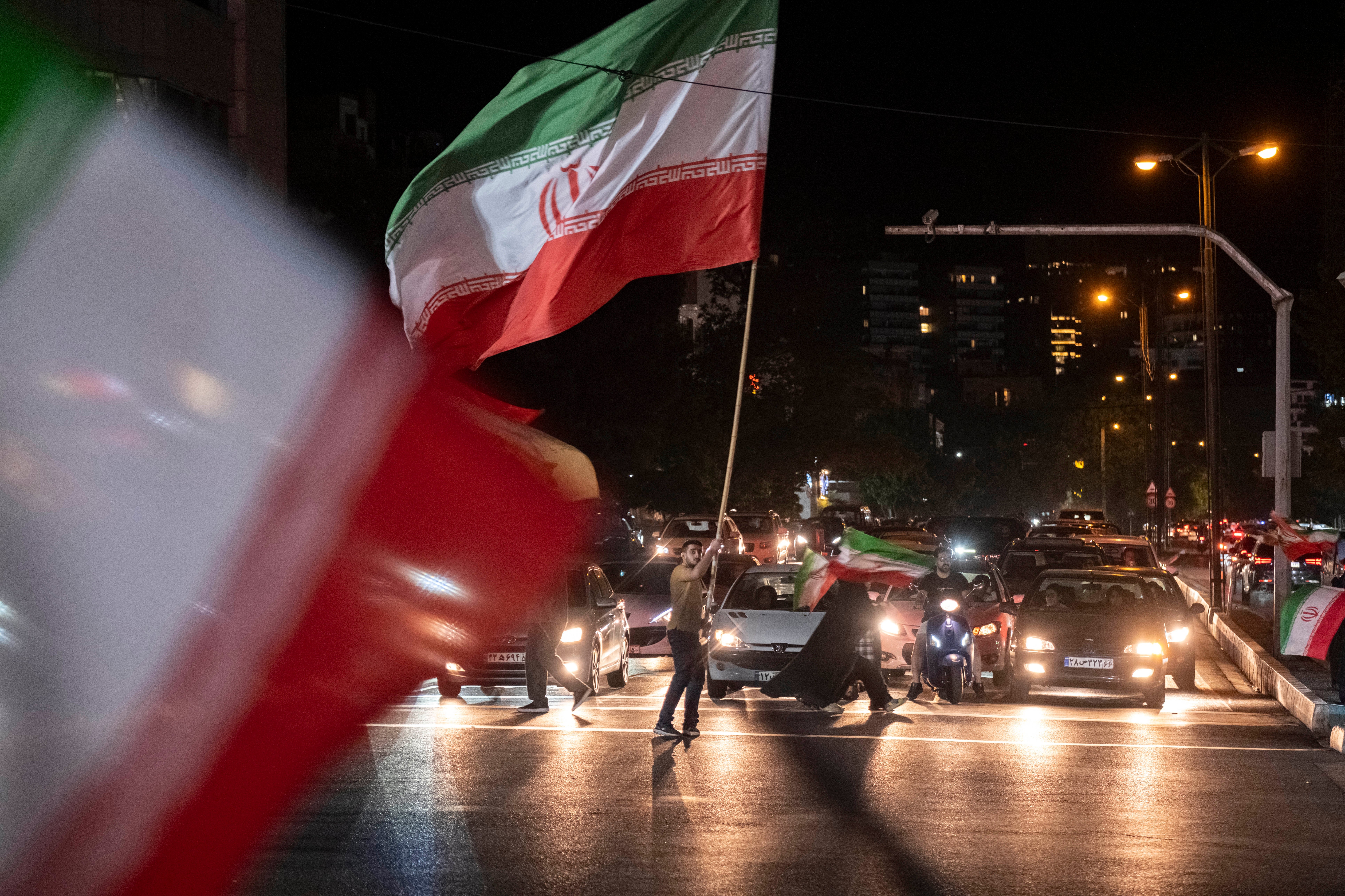 People question ample flags connected a metropolis thoroughfare astatine night, surrounded by cars and motorbikes
