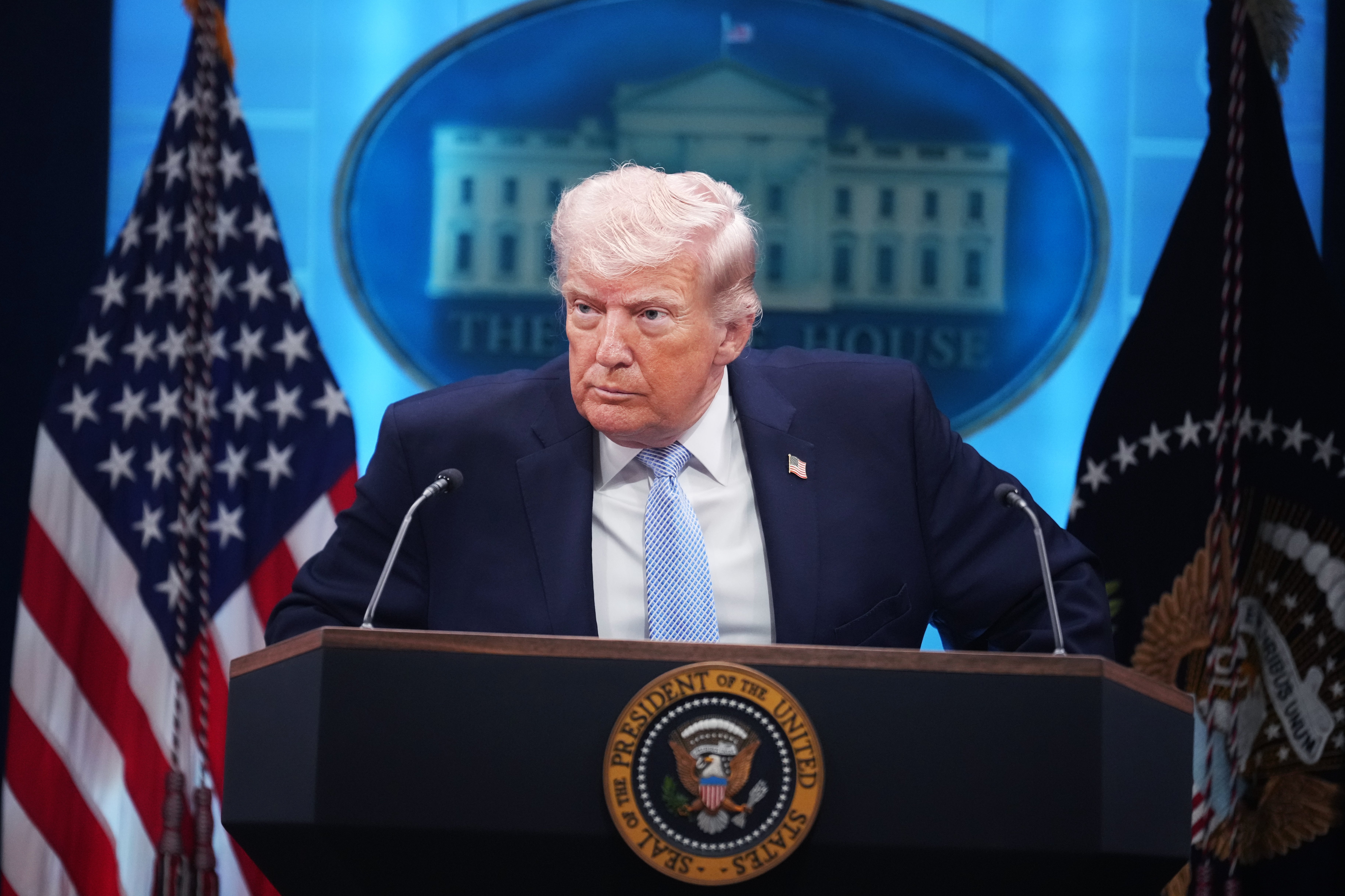 A idiosyncratic stands astatine a podium with U.S. flags and a statesmanlike seal, looking serious