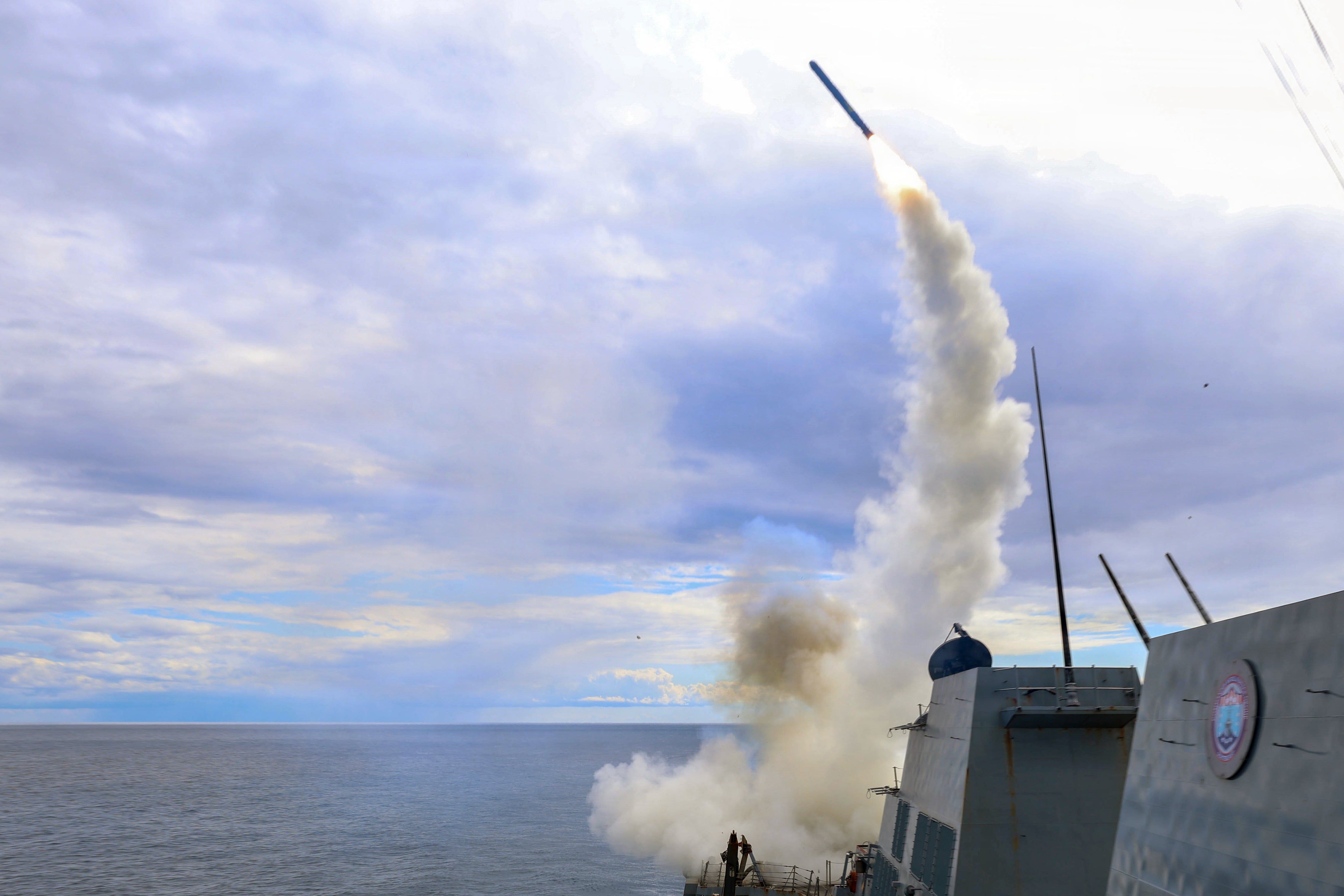 A rocket is launched from a naval vessel astatine sea, with fume trailing down it, nether a cloudy sky