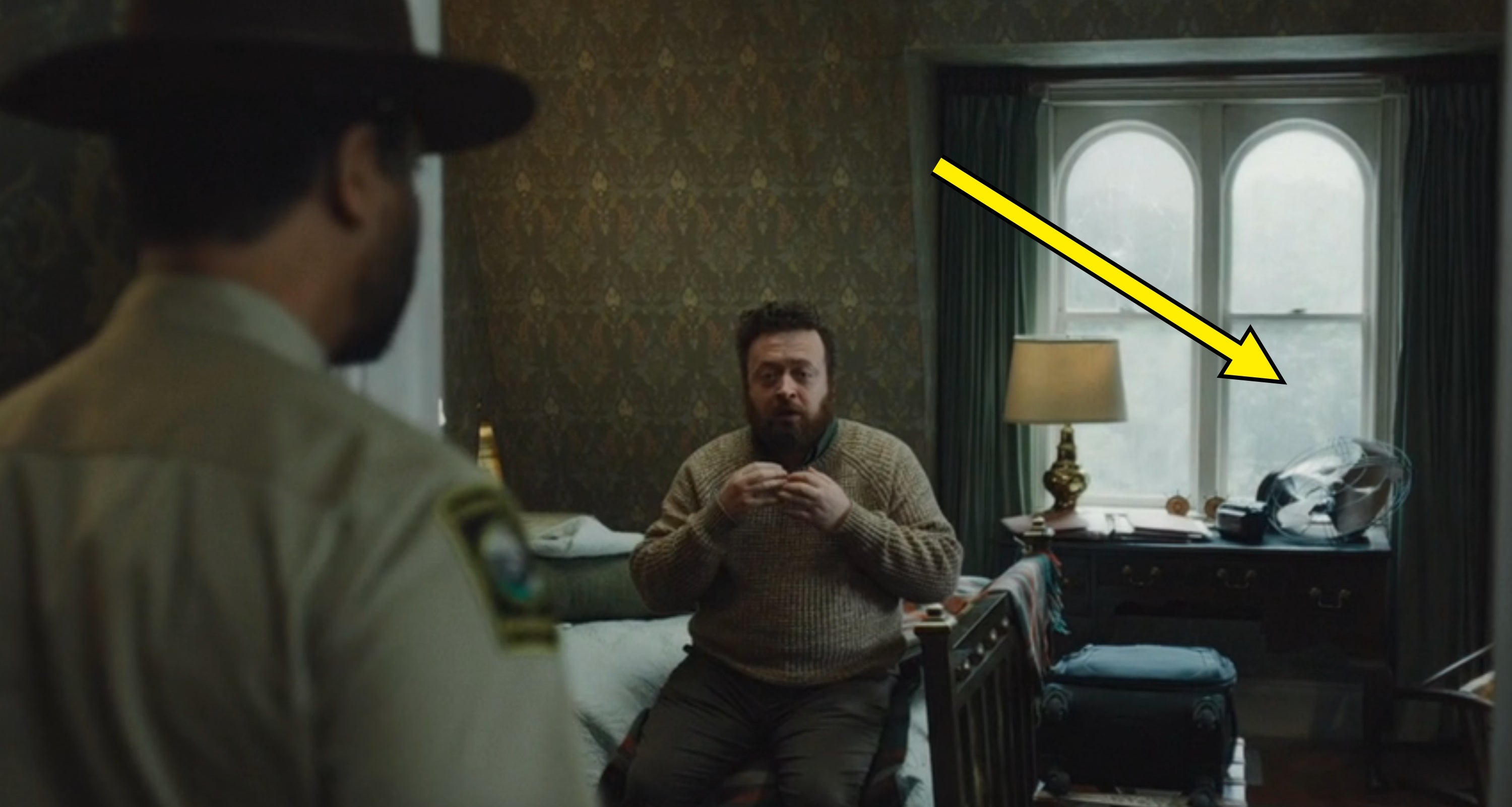 A antheral   sits connected  a furniture  successful  a dimly lit room, speaking to a idiosyncratic   successful  a sheriff's uniform, who stands with their backmost  to the camera
