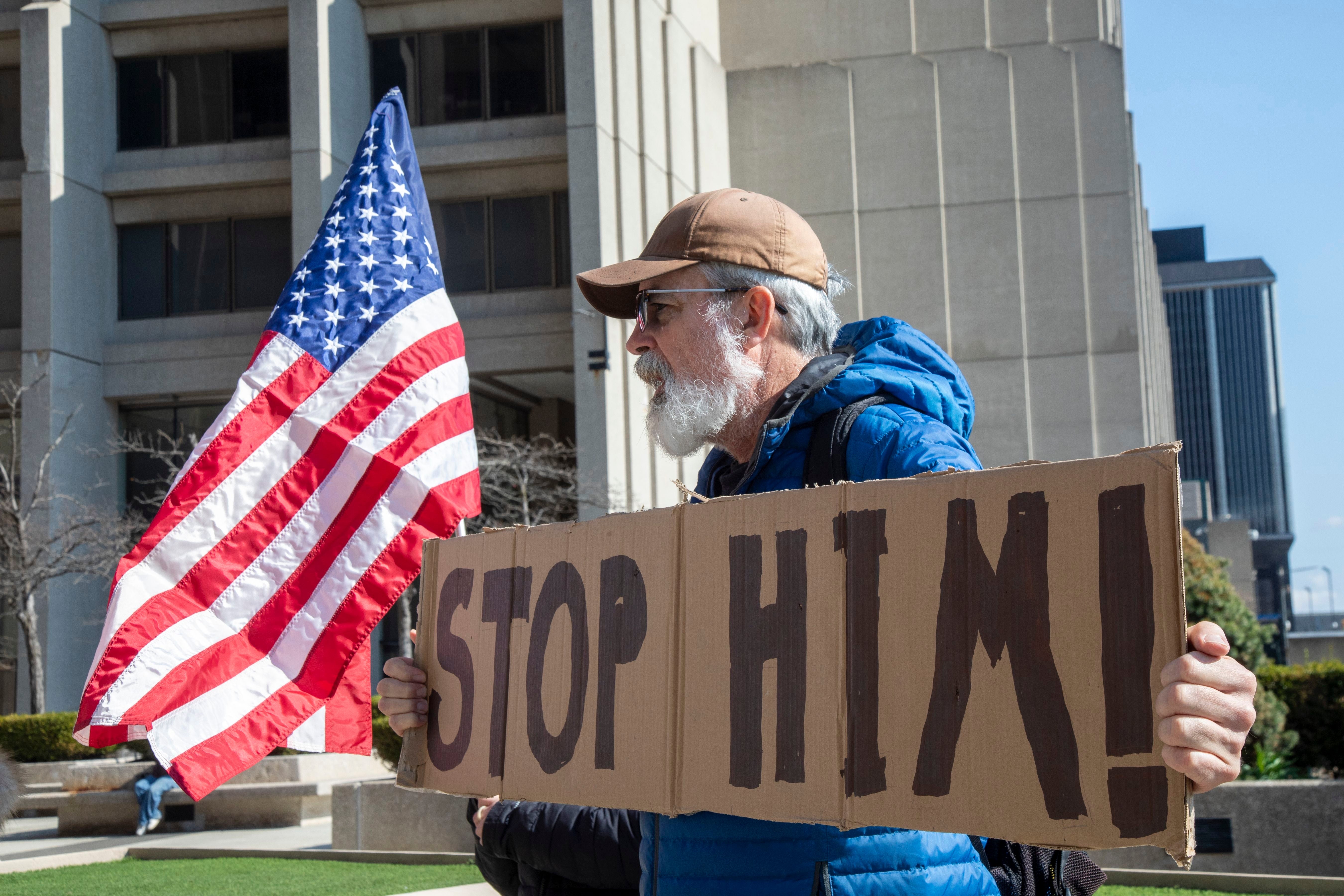 Man with a beard holds a "Stop Him!" motion successful a nationalist protest, carrying an American flag