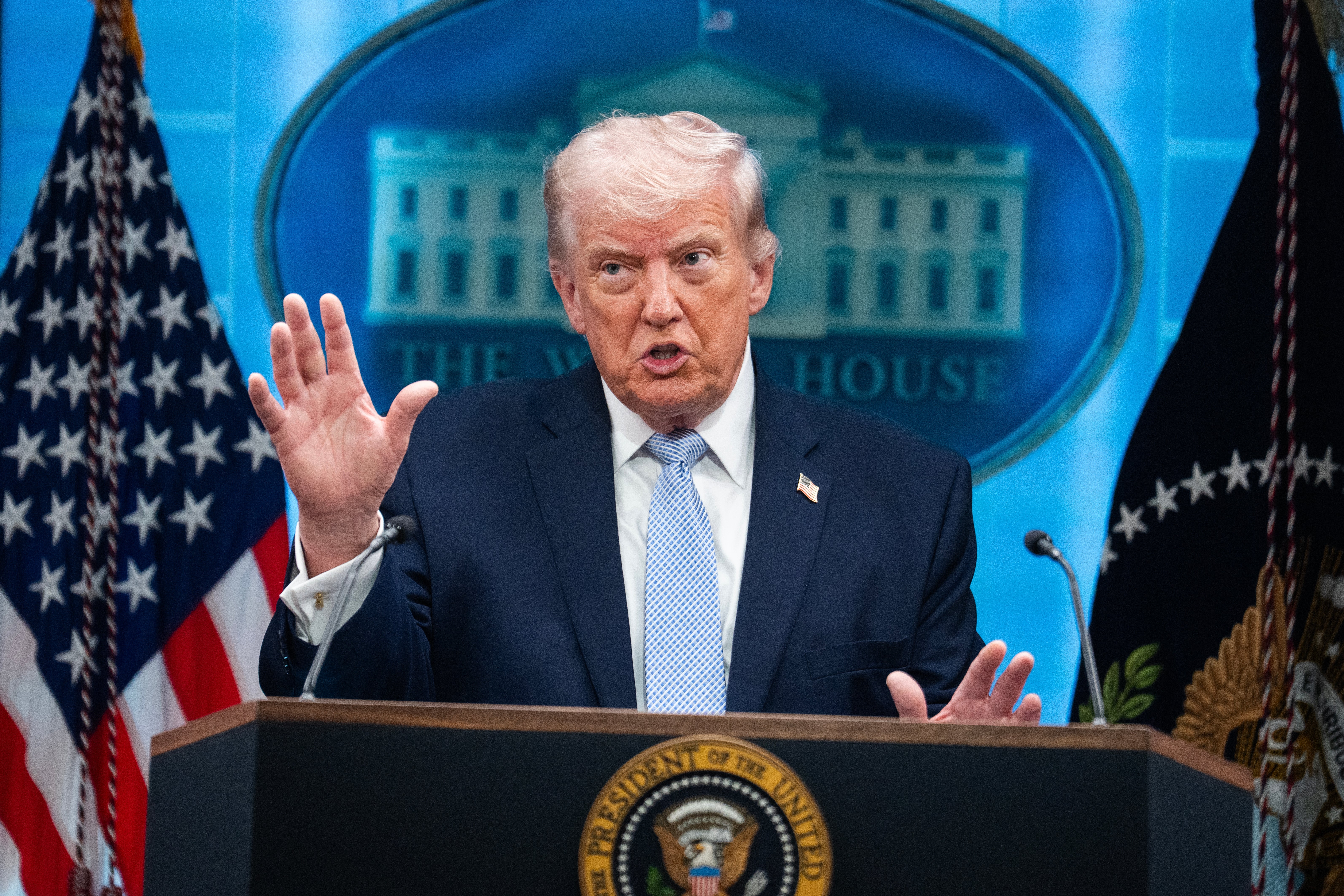 A idiosyncratic astatine a podium with the Presidential Seal gestures portion speaking, with flags and a inheritance representation of a gathering emblem