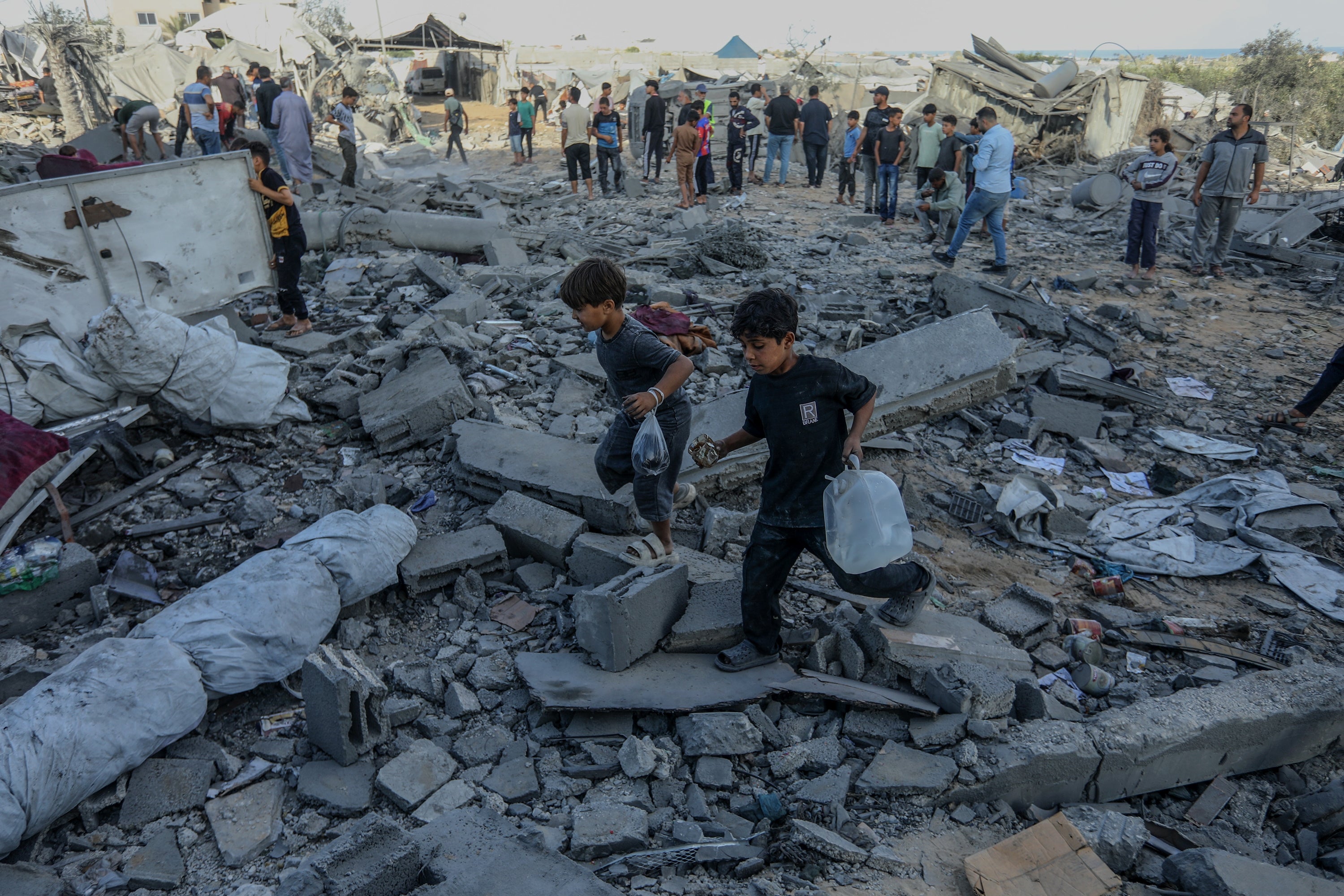 Children carrying h2o navigate rubble from destroyed buildings; a assemblage stands successful the inheritance among debris