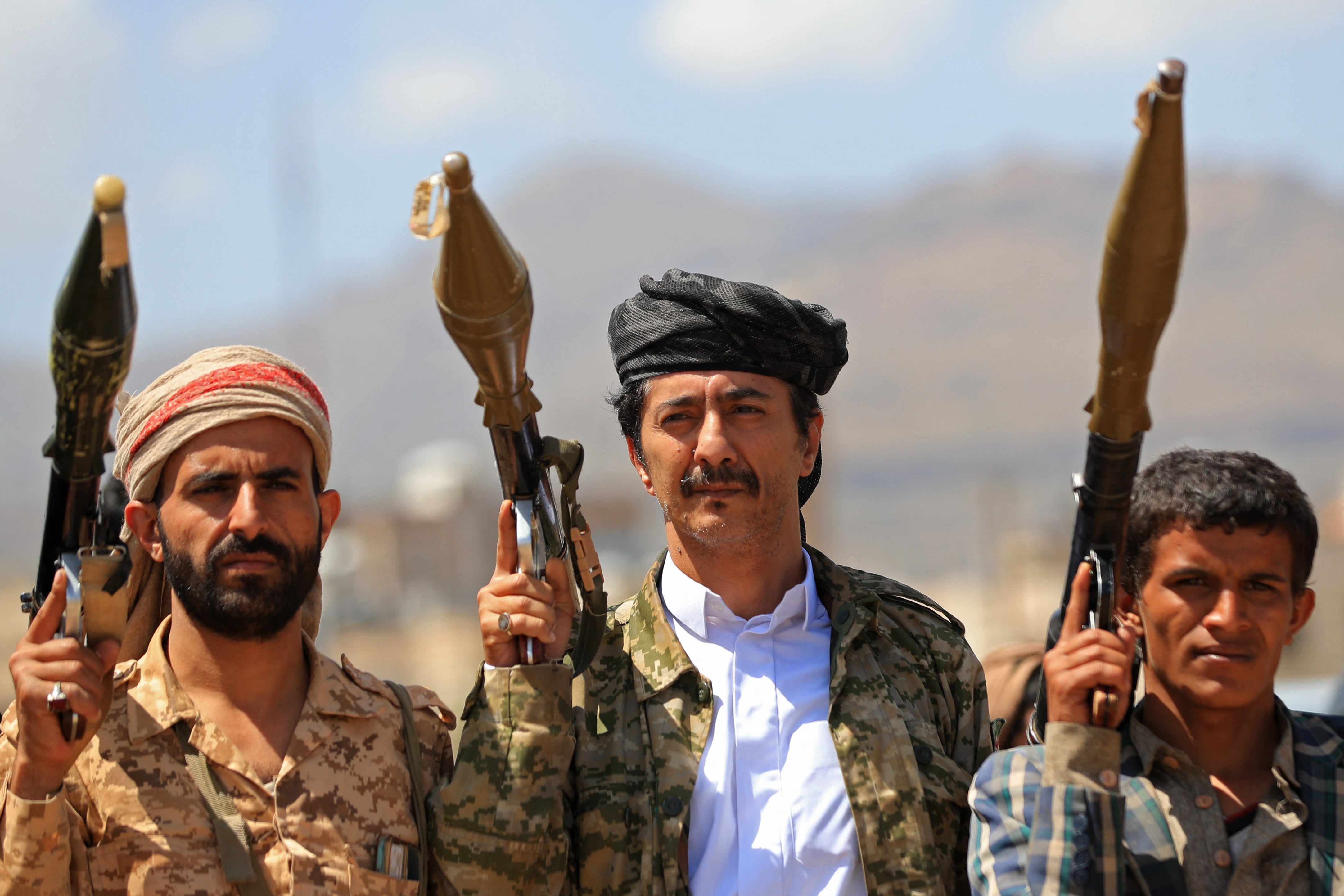 Three men holding weapons basal outdoors, wearing accepted and military-style clothing