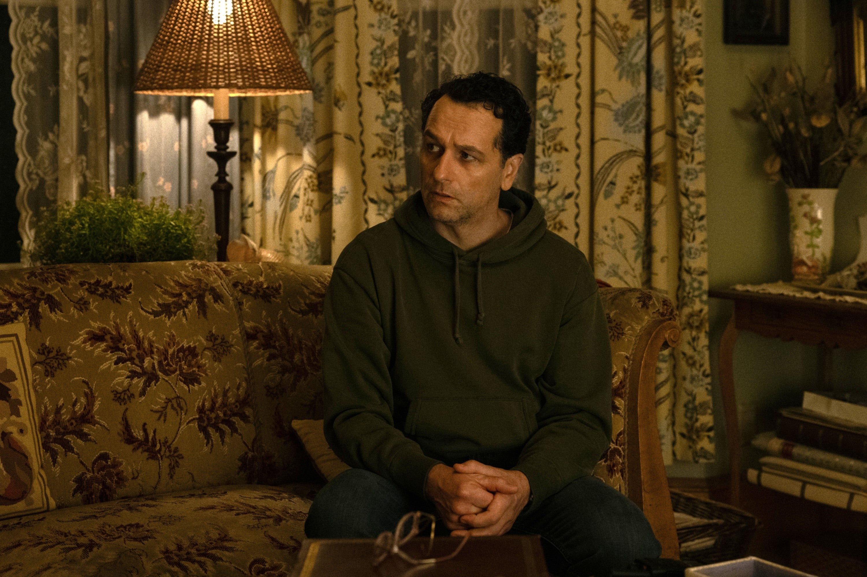 Person sitting connected  a patterned sofa  successful  a cozy, vintage-style room, looking to the broadside  with a contemplative expression