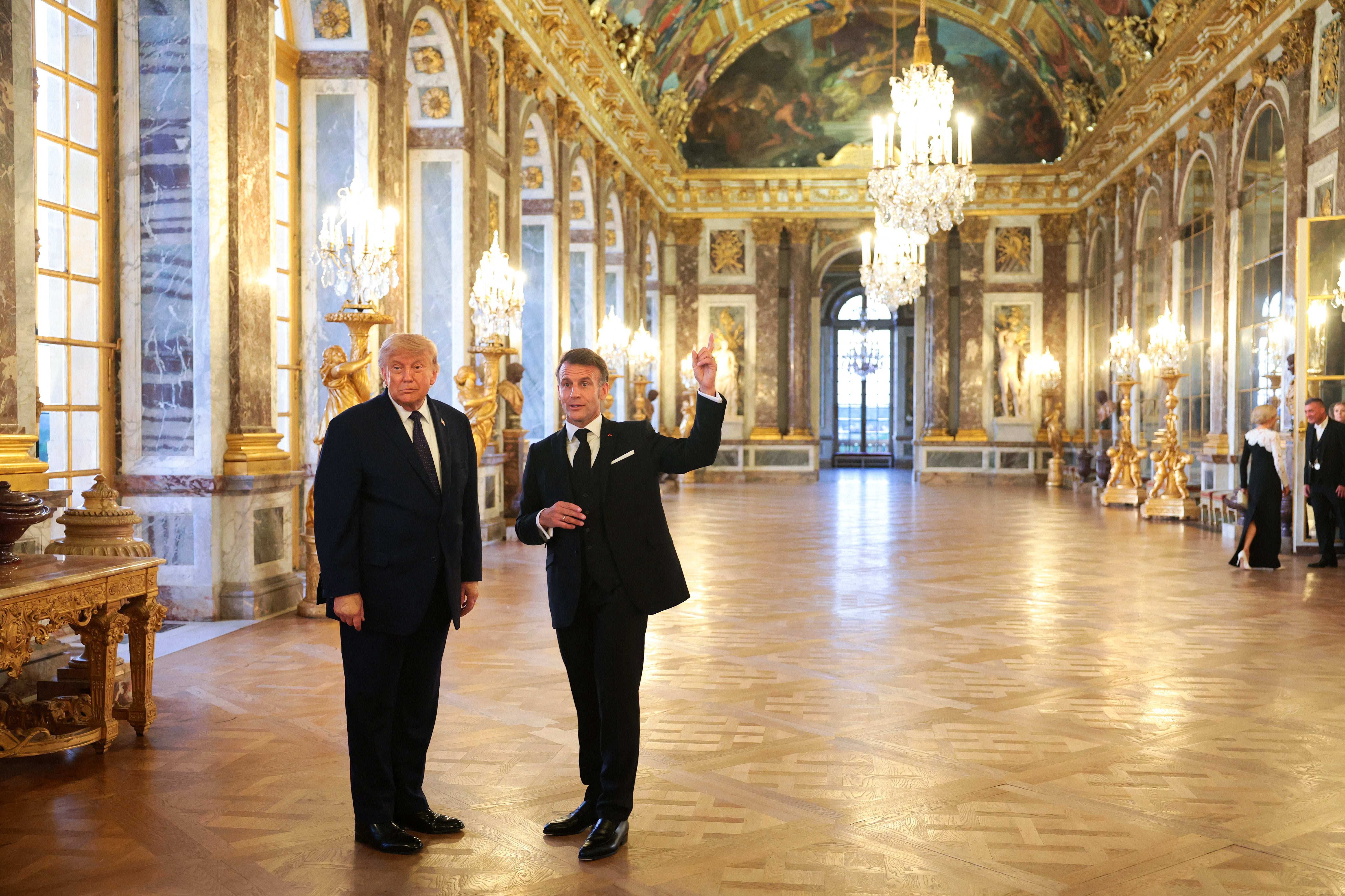 Two men successful ceremonial suits basal successful the opulent Hall of Mirrors astatine the Palace of Versailles, with chandeliers and ornate decor successful the background