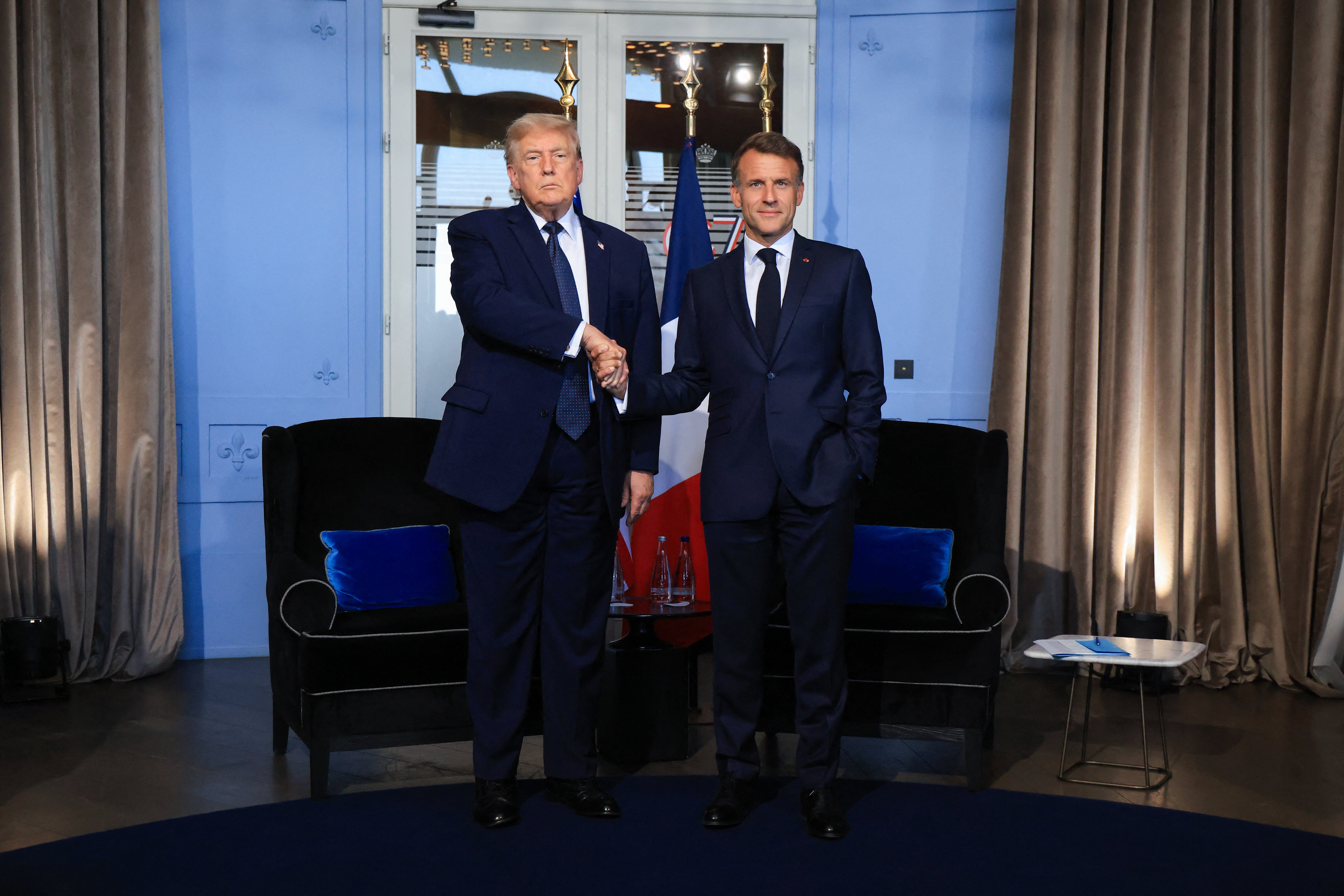 Two suited individuals shingle hands successful a ceremonial setting, lasting successful beforehand of a flag
