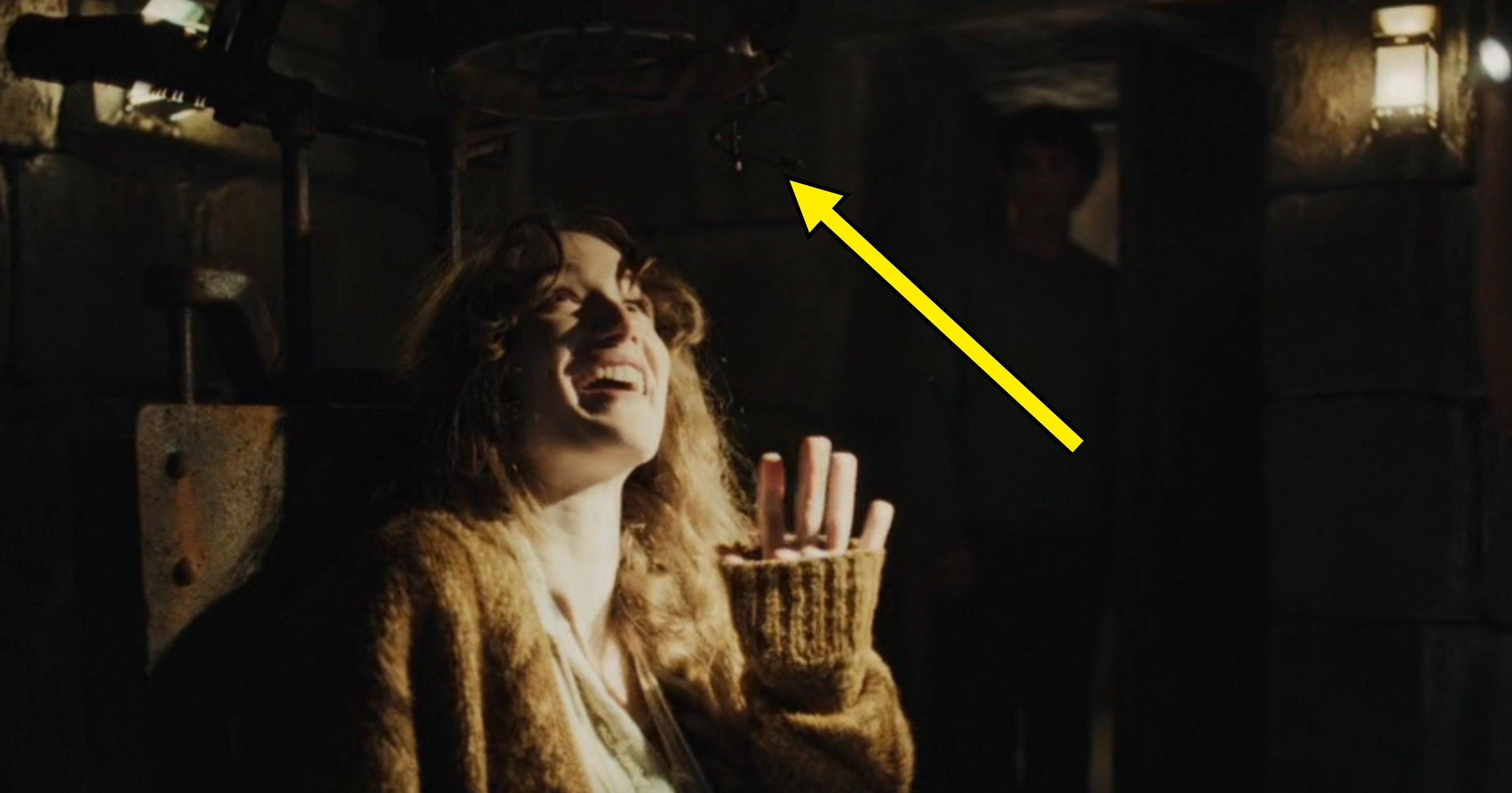 A idiosyncratic   smiles warmly successful  a dimly lit room, gesturing upwards. Another fig  stands successful  the background