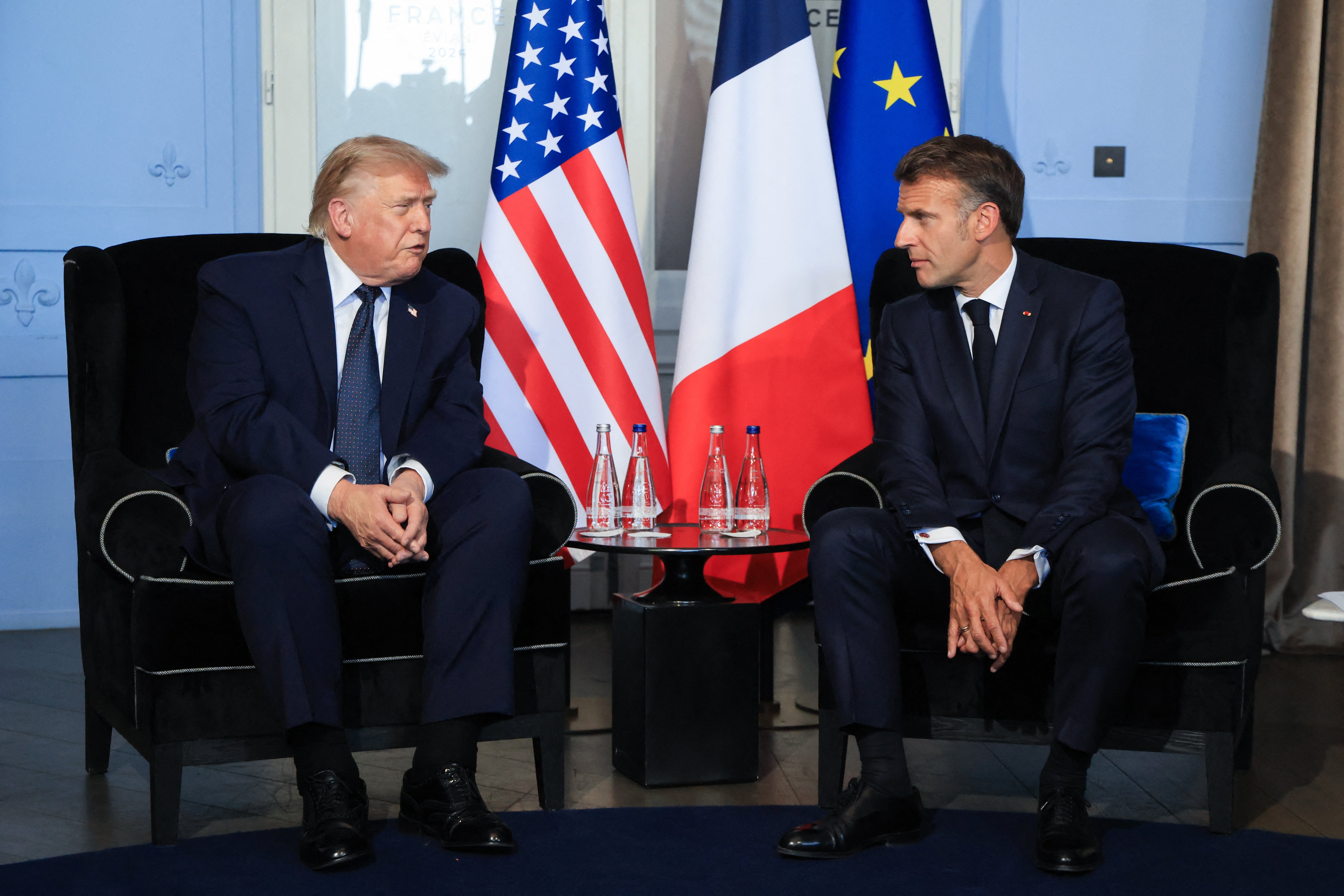 Two men successful suits beryllium connected chairs with U.S. and French flags down them, engaged successful conversation
