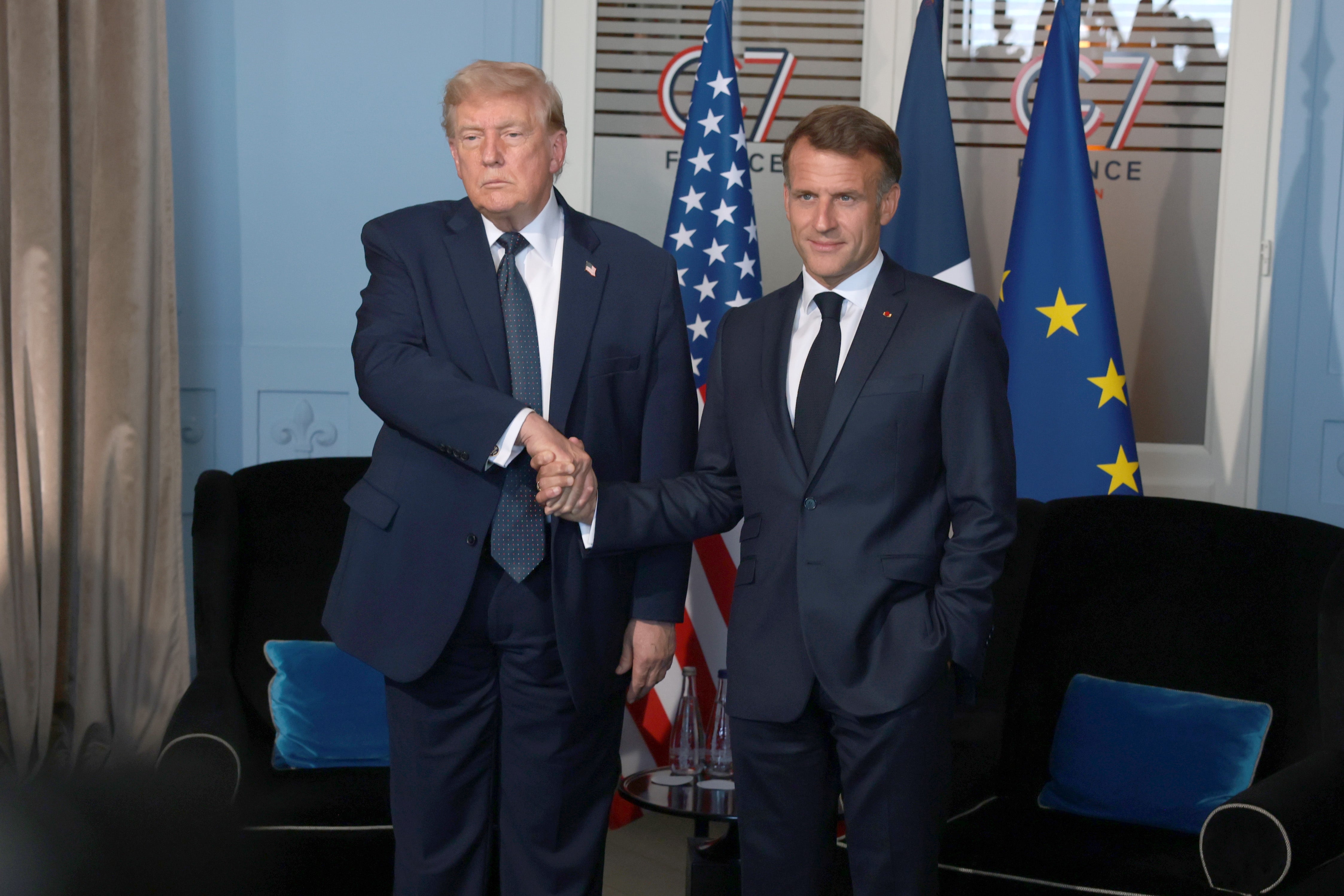 Two men successful suits shingle hands astatine a ceremonial event, with flags and a G7 logo successful the background