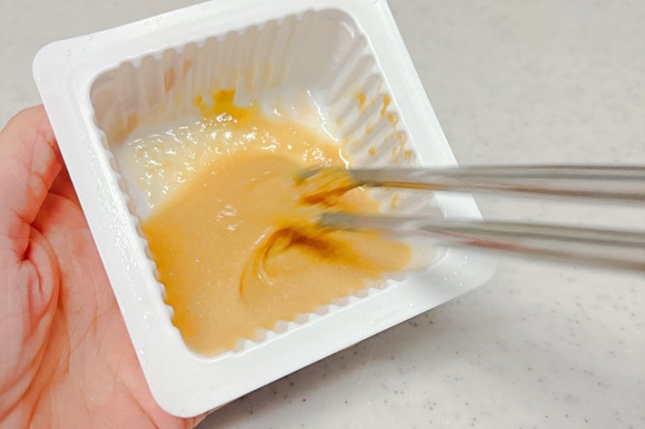 手に持った容器の中で箸を使って納豆を混ぜている様子。