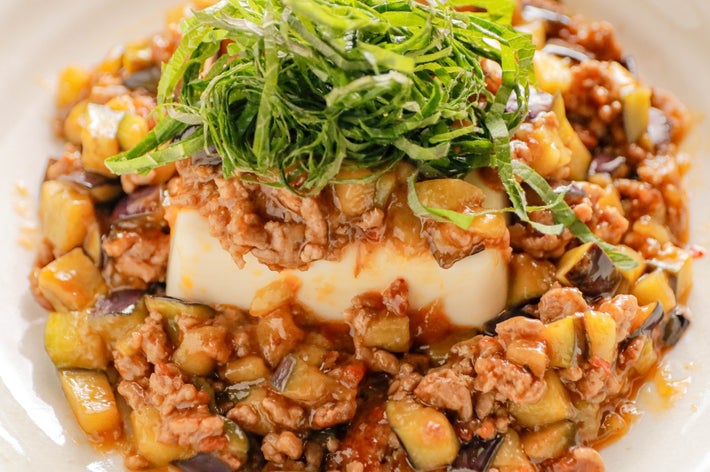 絹豆腐の上に、なすと豚ひき肉のピリ辛そぼろあん、千切りの大葉がトッピングされている料理